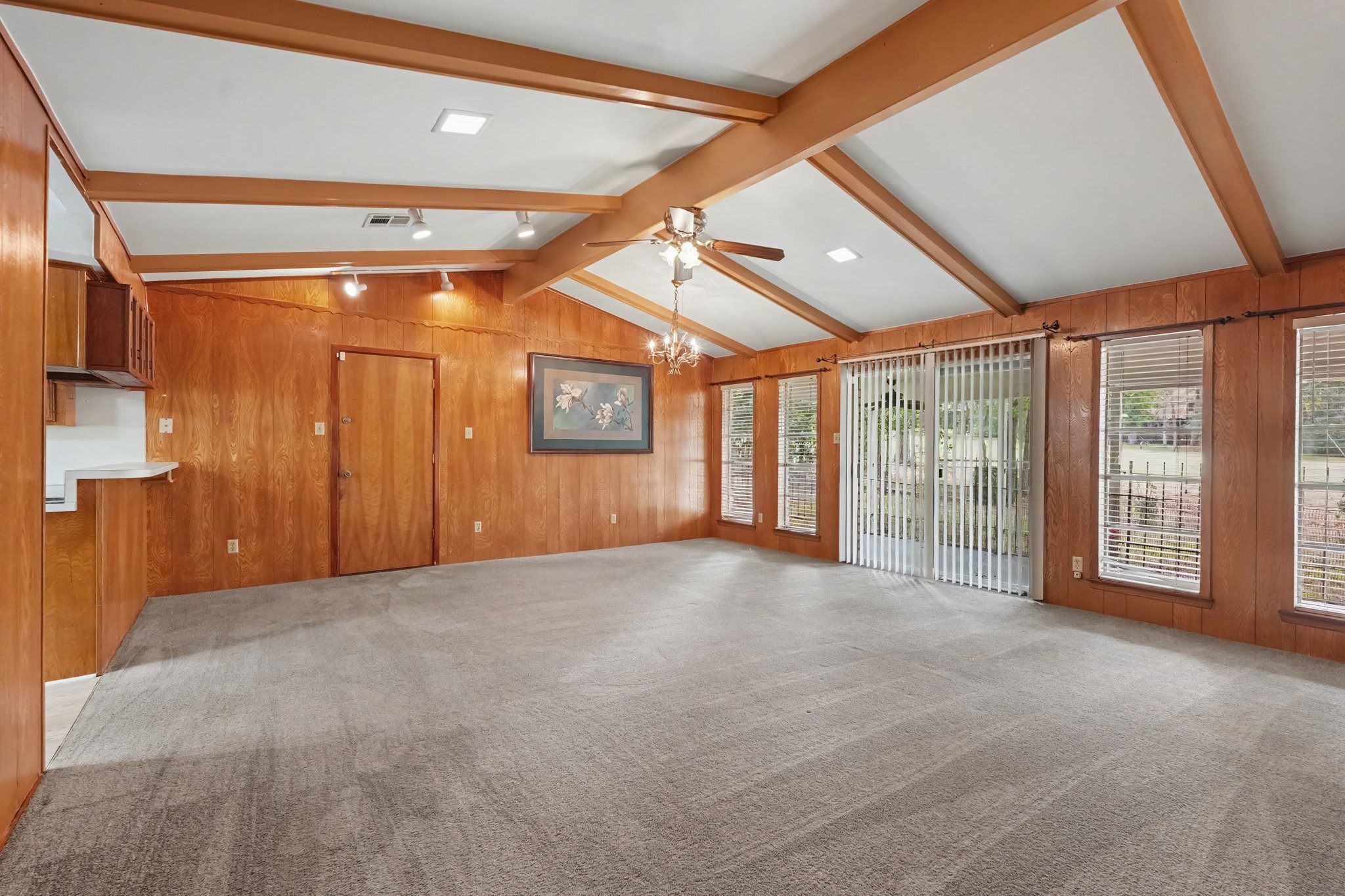 Spacious family room featuring vaulted beamed ceilings, a wall of oversized windows with scenic views, and seamless outdoor access through sliding glass doors. This inviting space is finished with comfortable carpeting throughout, making it an ideal setting for both relaxing with family and hosting guests.