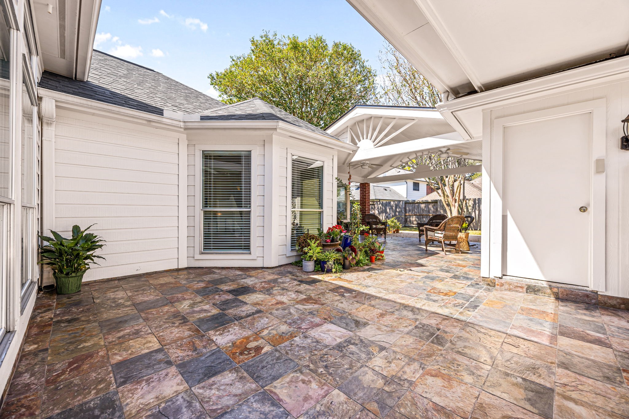 The covered back patio features a beautiful tiled floor and a charming sunburst gable detail, creating a warm, inviting space to relax outdoors.