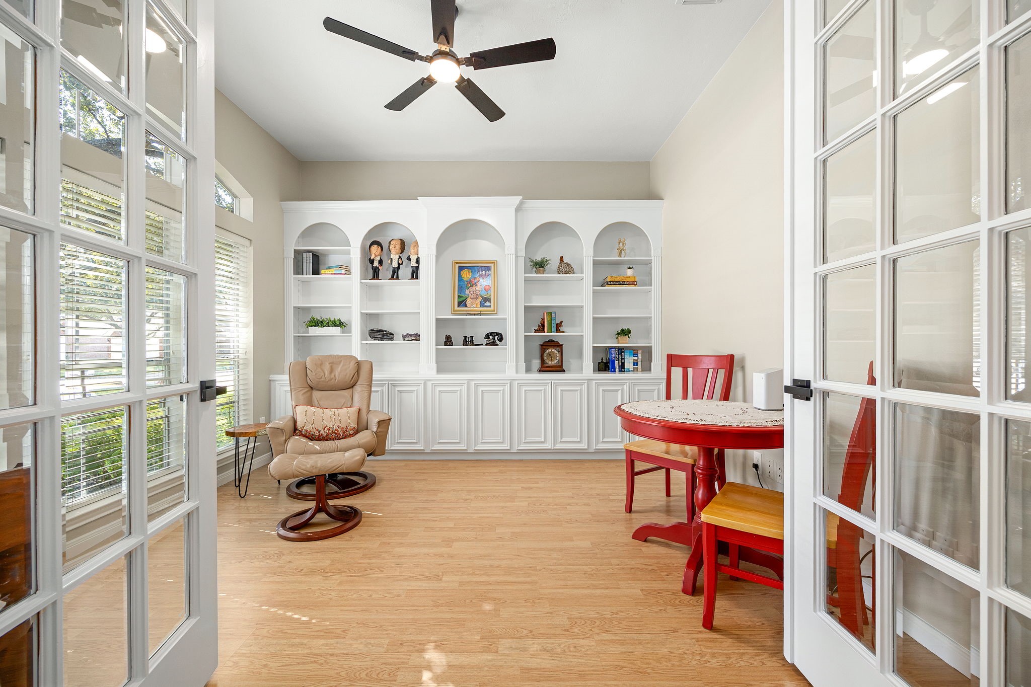Just off the foyer, a private home office features a ceiling fan and custom built-in bookcase with arched niches, framed by elegant French doors.