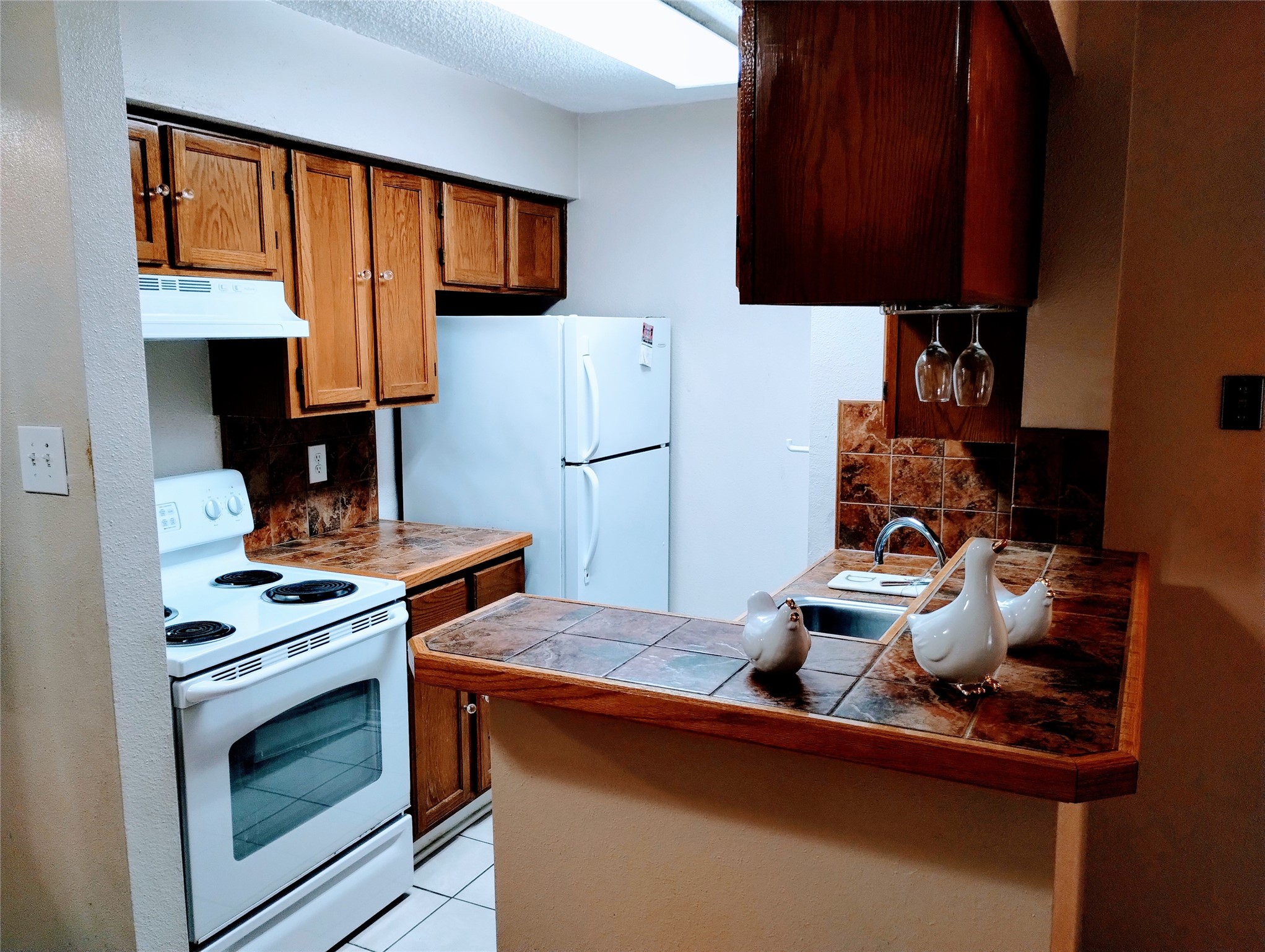 The charming KITCHEN has ample cabinetry, tiled countertops, and white appliances including a refrigerator, electric range with a vent hood, and a dishwasher.