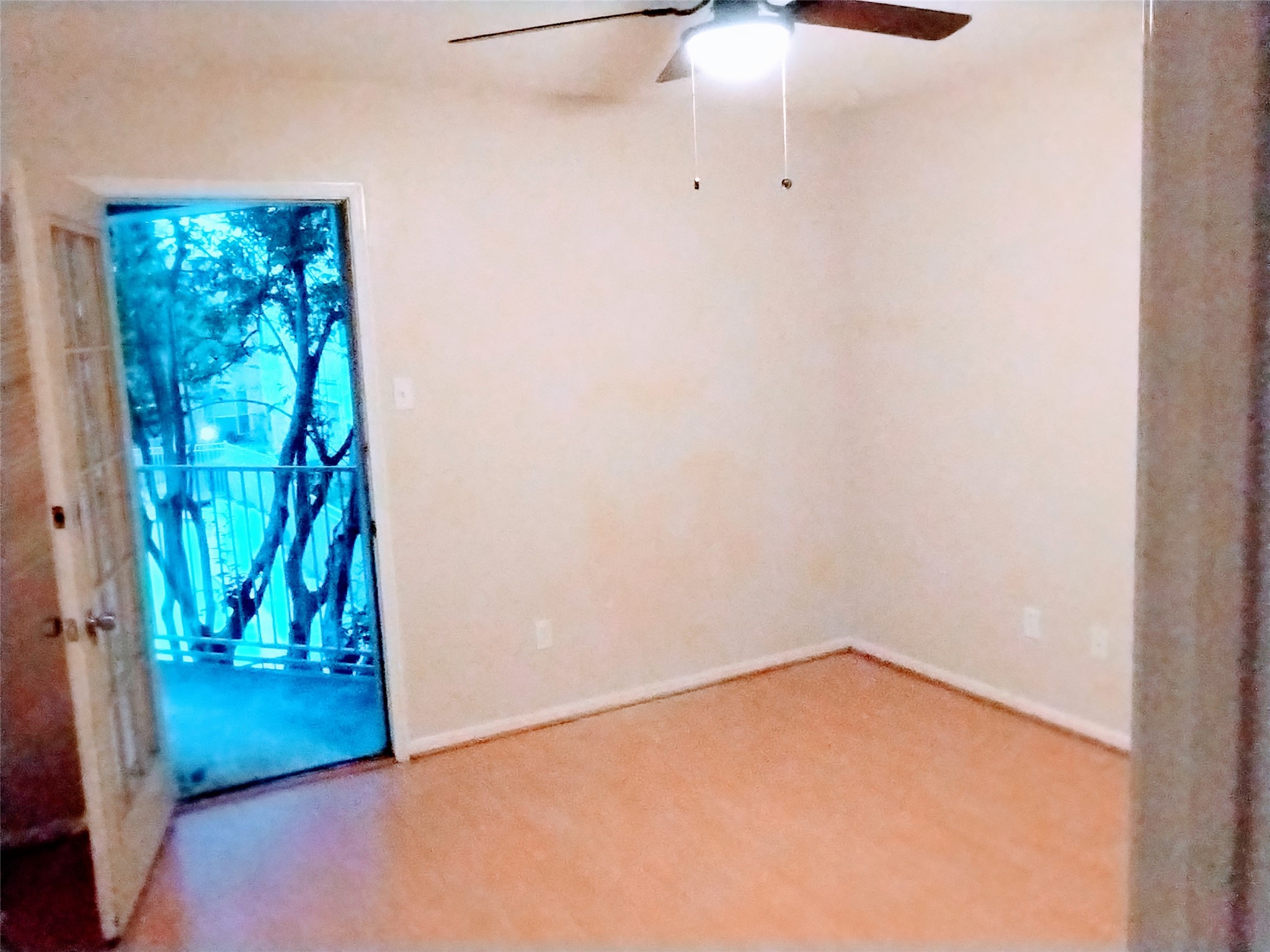 The PRIMARY BEDROOM features laminate flooring, neutrally-painted walls with white trim, a ceiling fan (with light), and an unseen walk-in closet.  There is a French door that opens to the BALCONY/TERRACE and offers lovely views of trees and the pool in the courtyard.