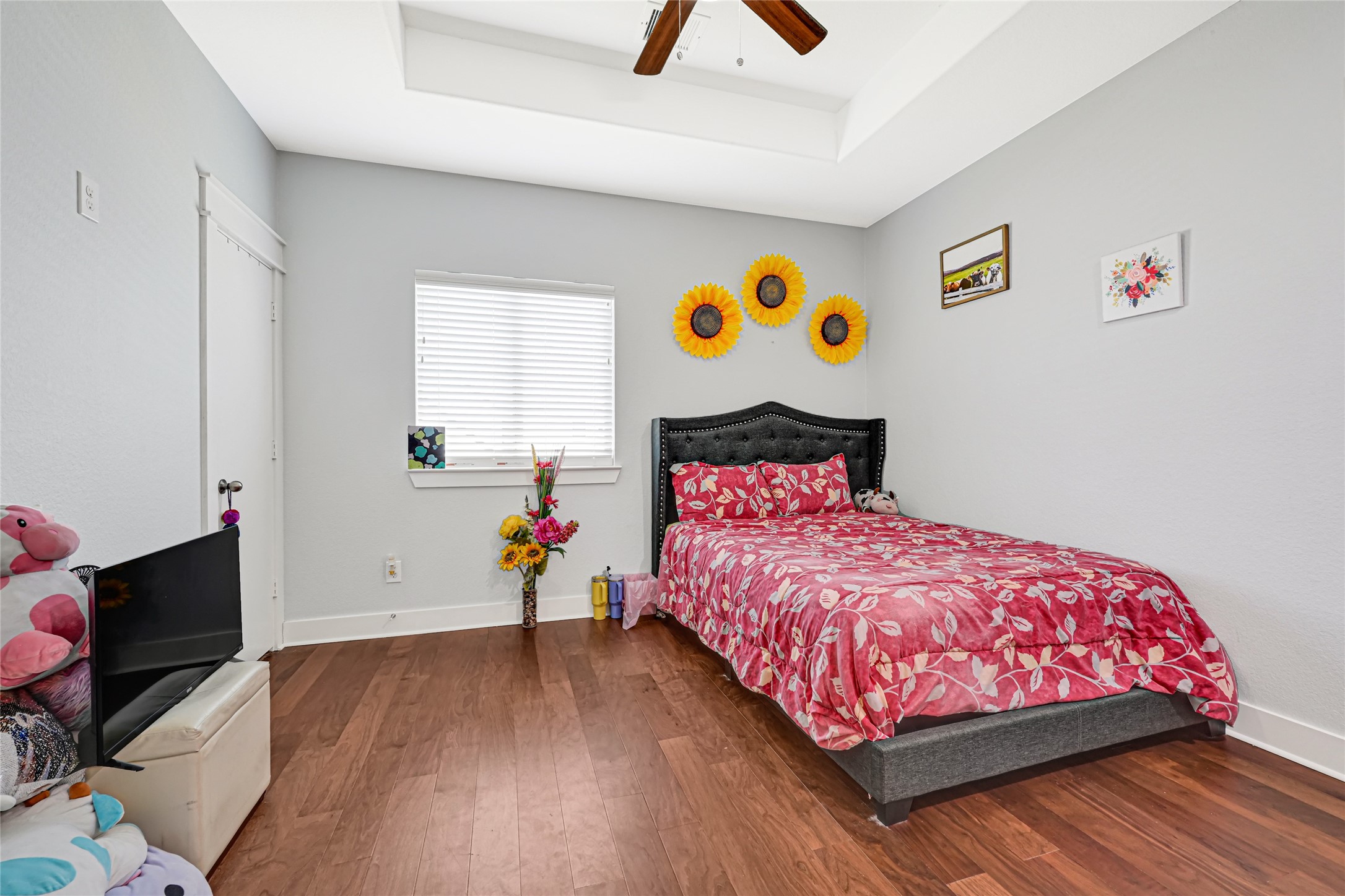 Inviting bedroom features wood flooring, a tray ceiling, and a window for natural light.