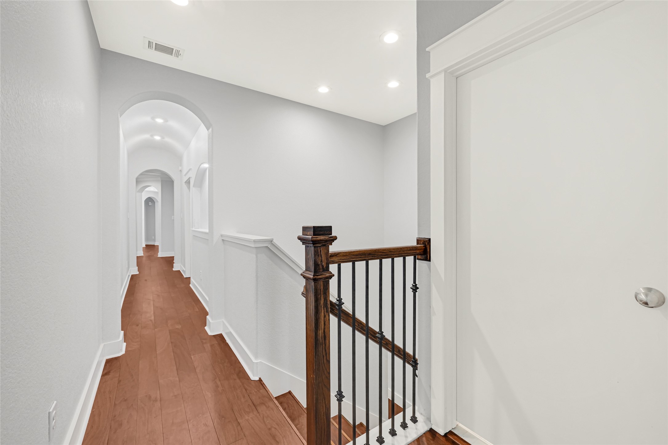 Upstairs hallway features wood flooring and decorative iron railing overlooking the staircase.