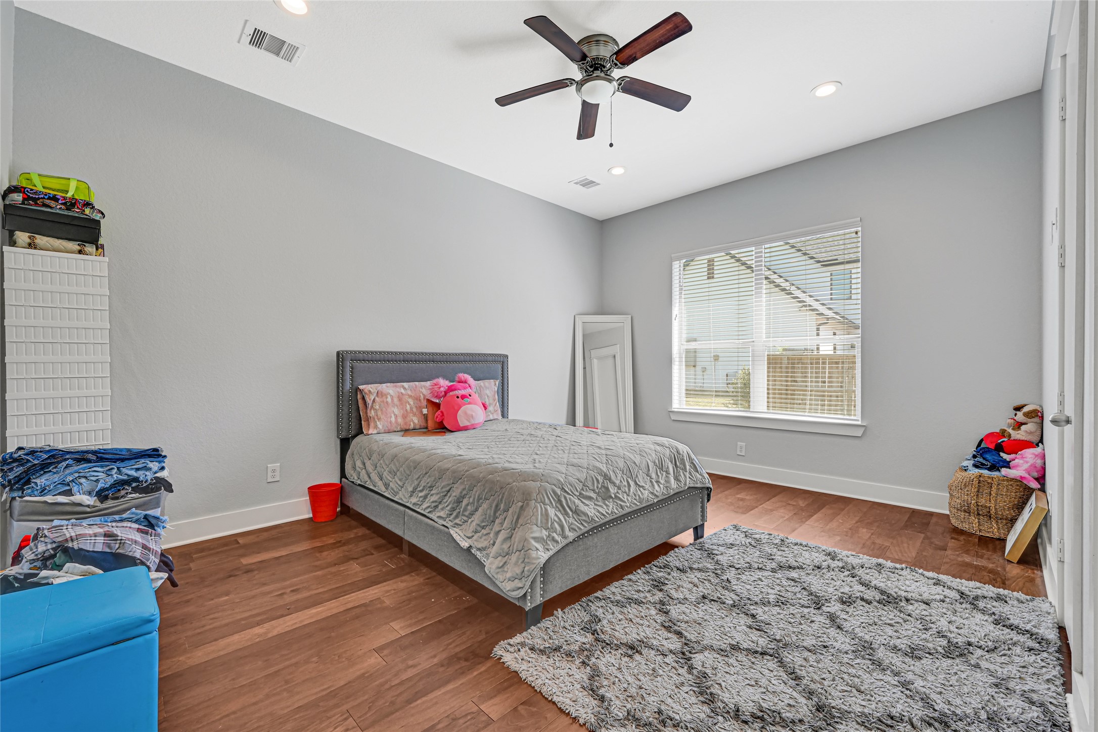 Spacious bedroom with wood flooring, a ceiling fan, and natural light.