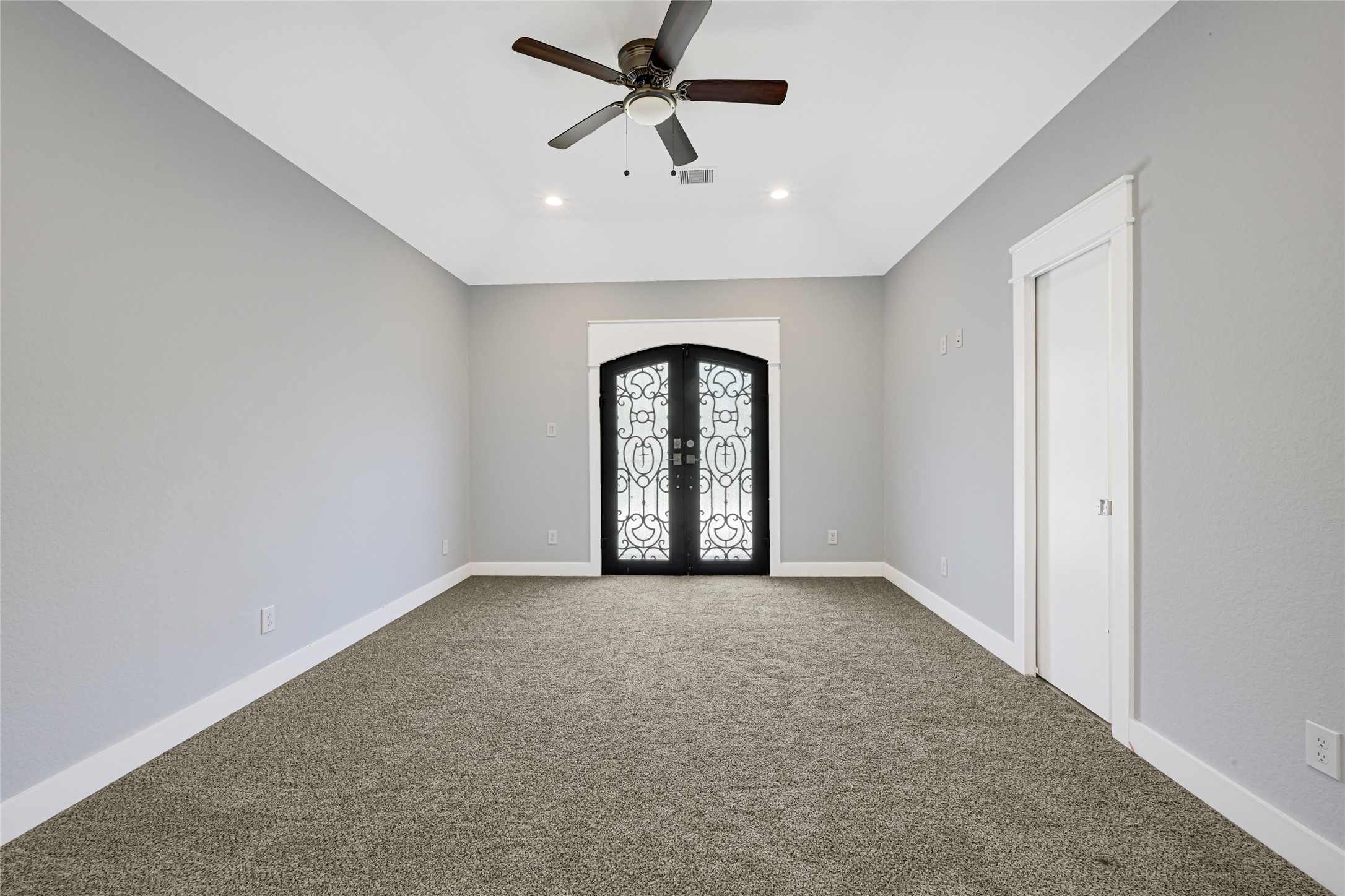 Carpeted room features a tray ceiling, ceiling fan, and glass-paneled double doors.