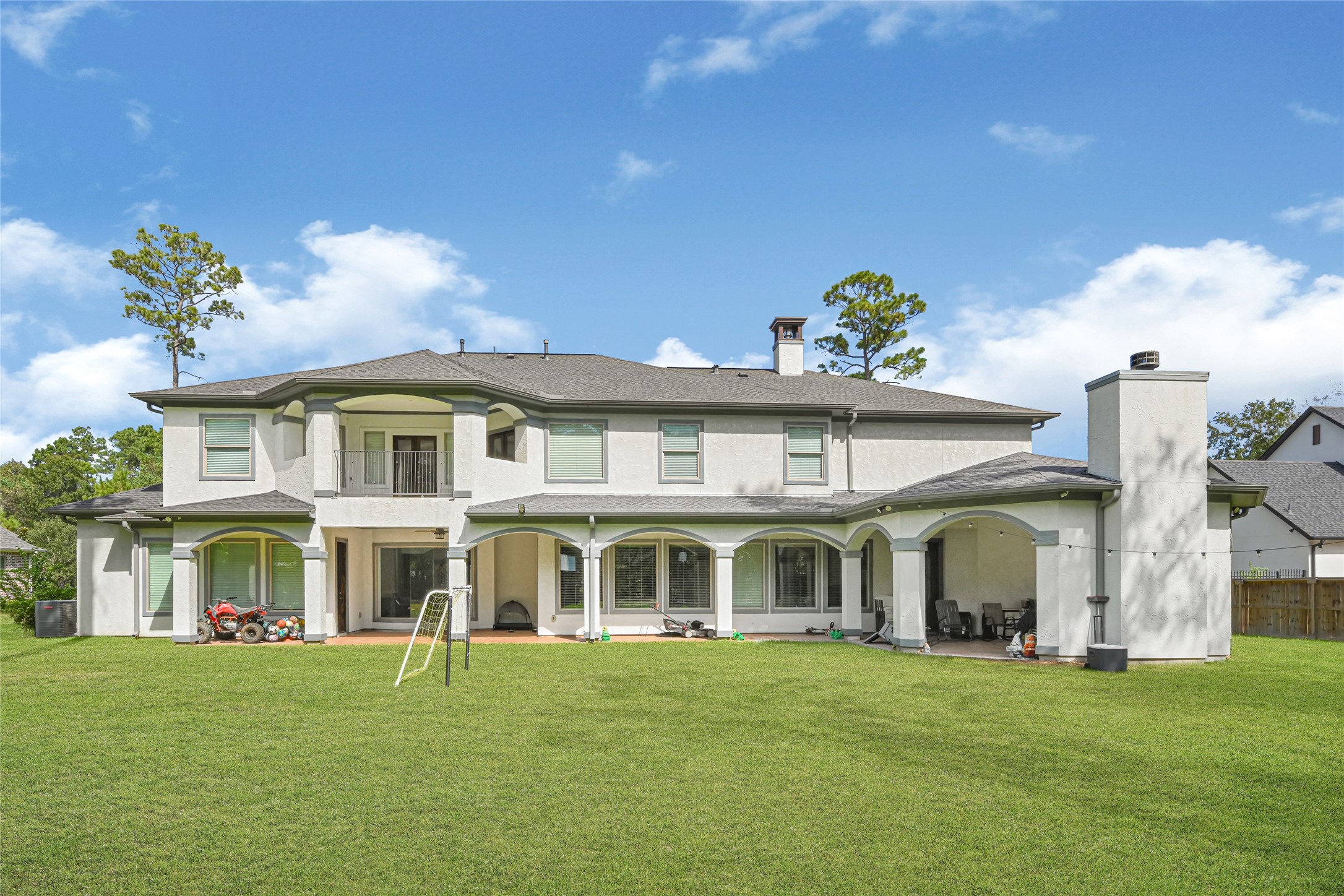 Rear exterior showcasing the covered patio, upstairs balcony, and spacious backyard.
