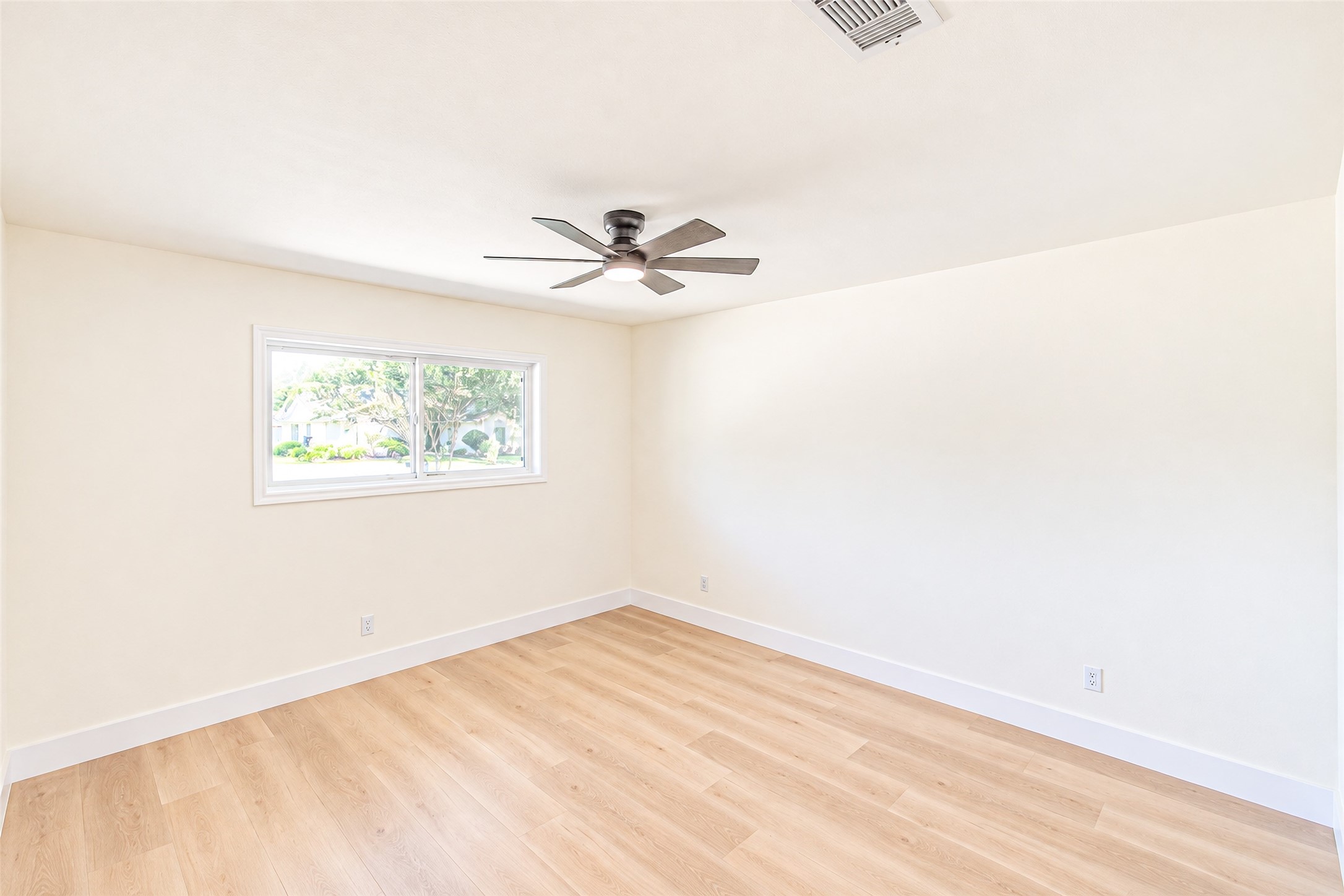 Bedroom 5 offers a spacious, sunlit retreat with sleek hardwood floors and a modern ceiling fan, perfect for relaxation and comfort.