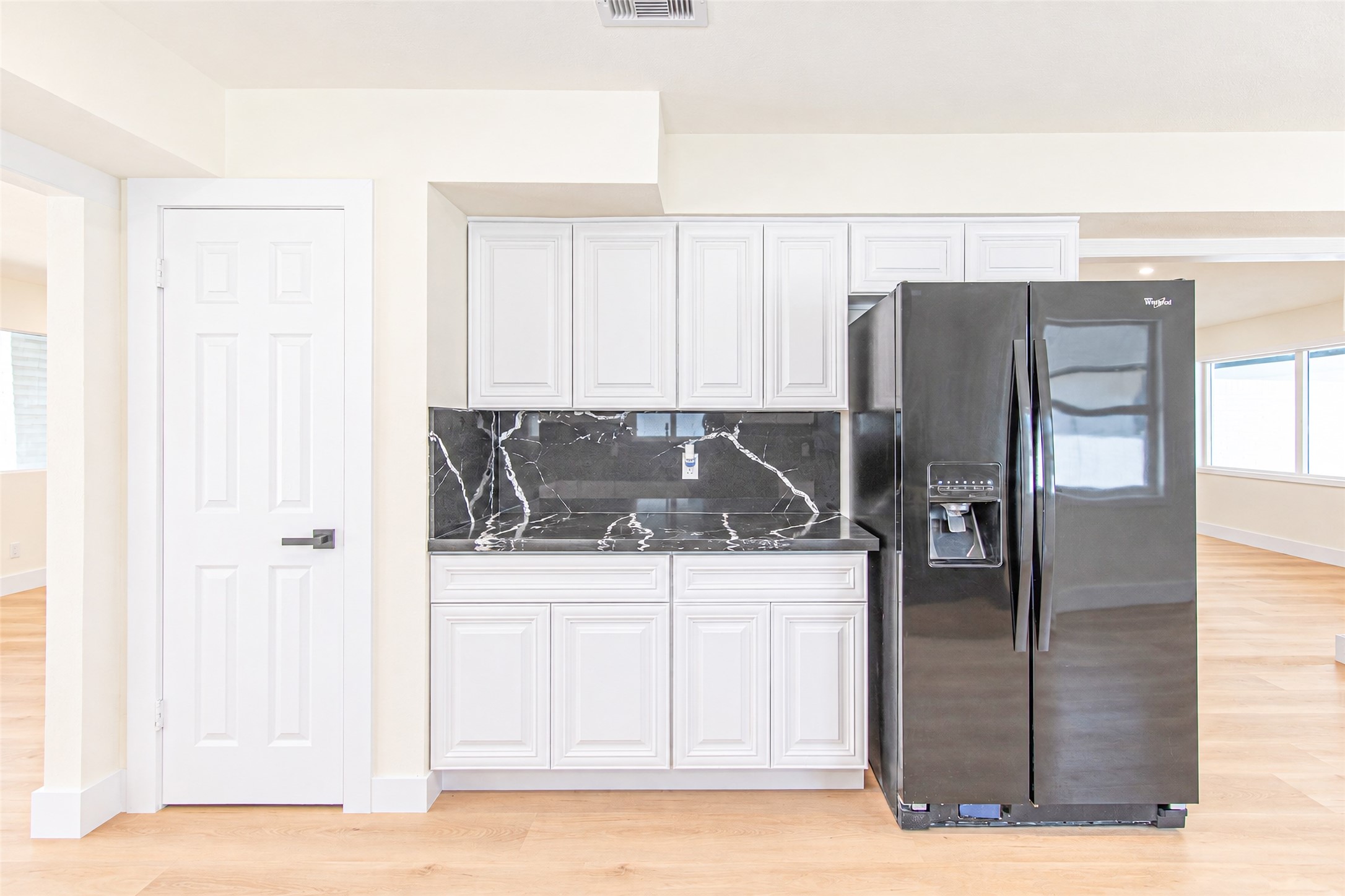 Experience modern elegance in this sleek kitchen, showcasing white cabinetry, a striking black marble backsplash, and a stainless steel refrigerator with a convenient water dispenser.