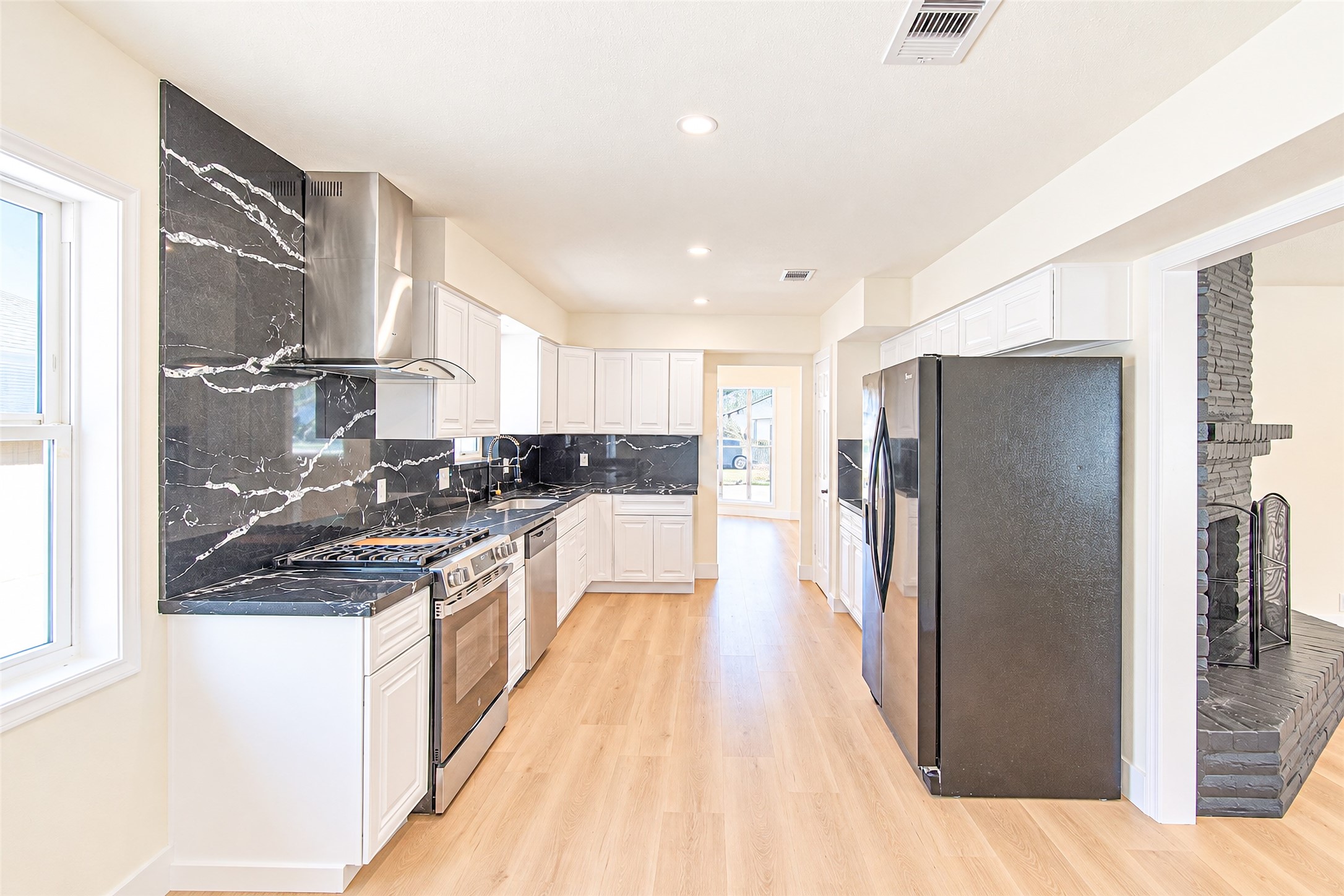 A sleek modern kitchen with elegant black marble countertops, stainless steel appliances, and crisp white cabinetry, enhanced by warm wooden flooring and abundant natural light.