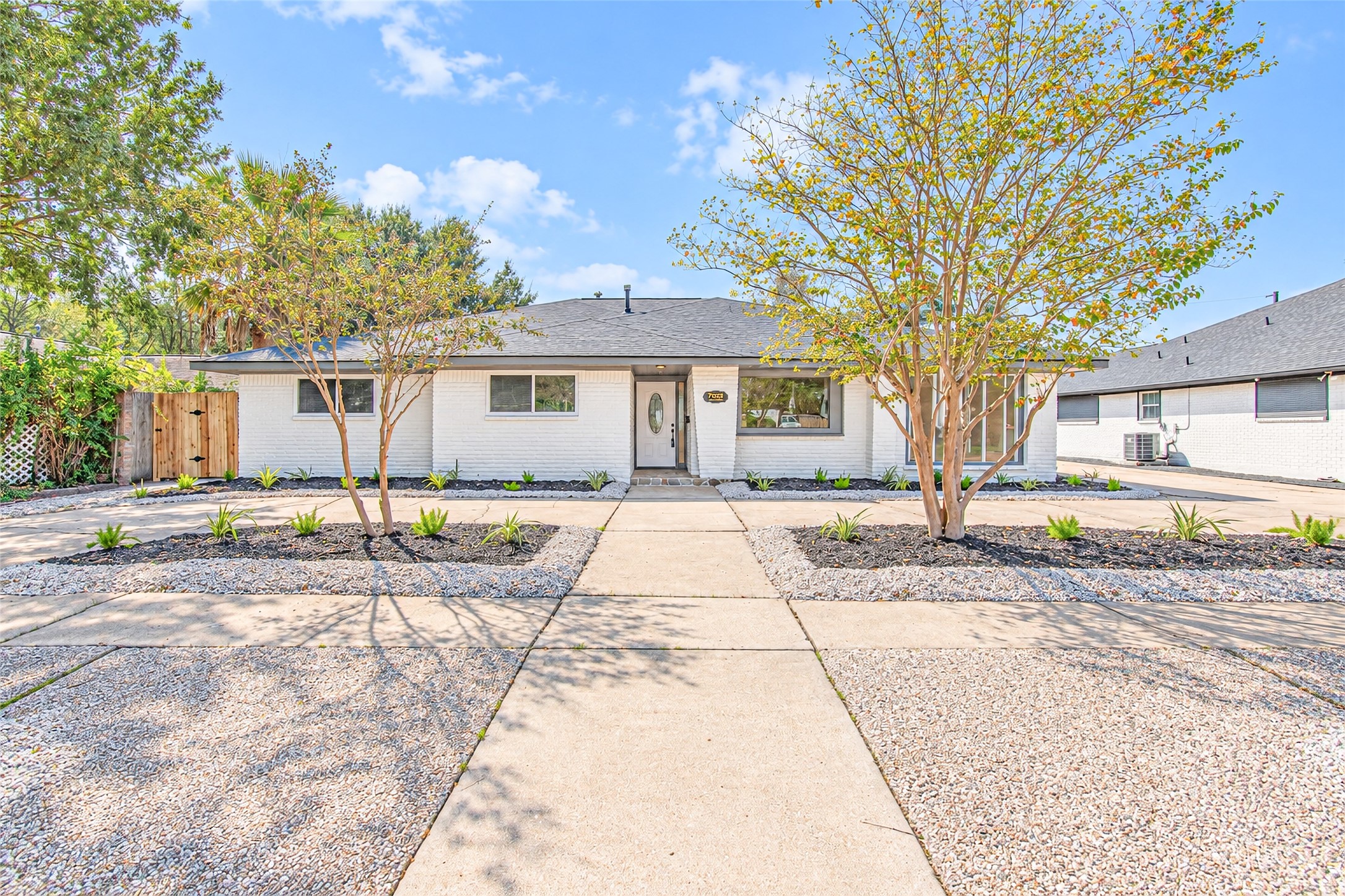 Charming single-story home with a modern facade, featuring a sleek white exterior and a spacious, low-maintenance front yard with stylish landscaping.