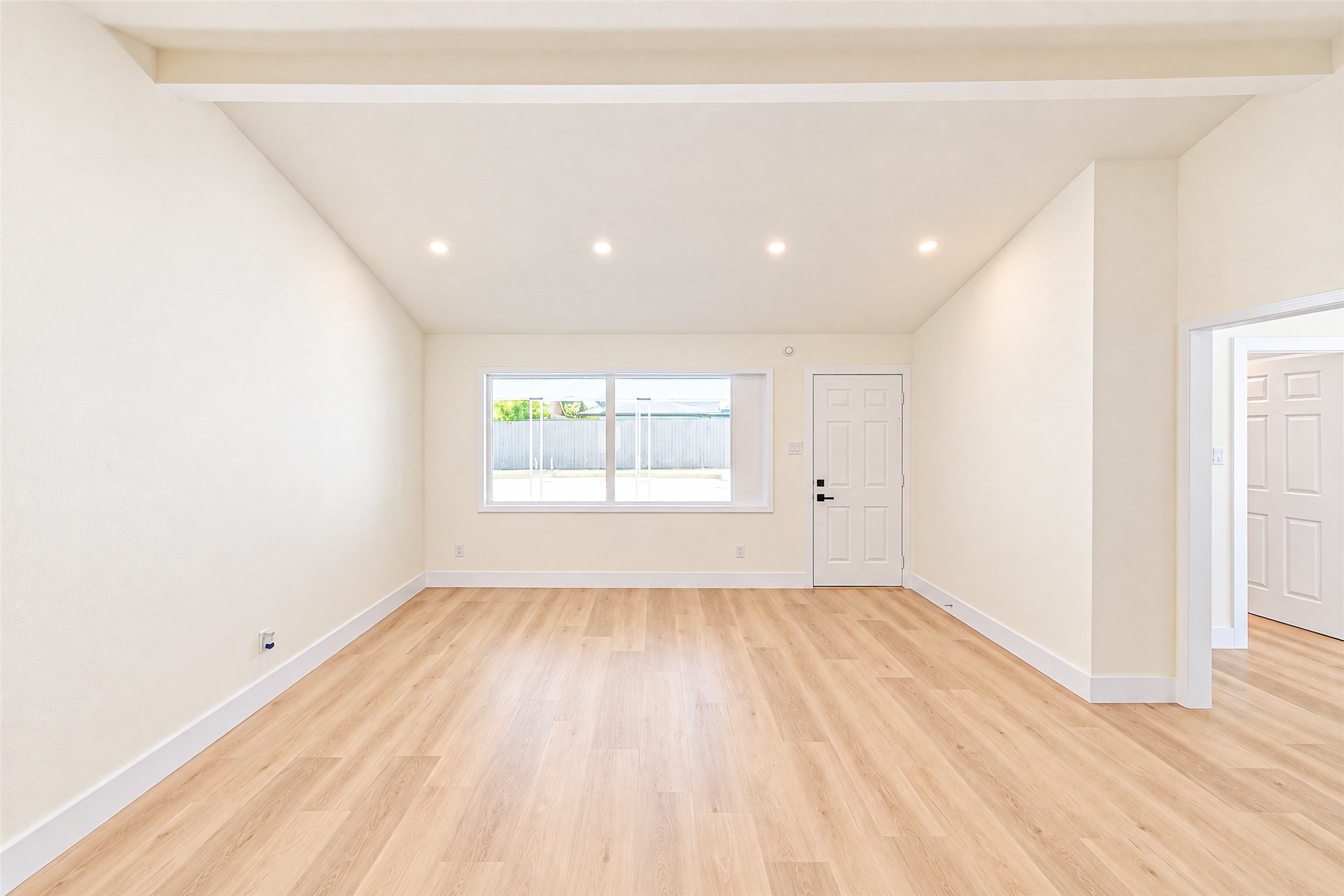 Discover a spacious living area with vaulted ceilings, sleek recessed lighting, and abundant natural light streaming through a large window, all beautifully complemented by light wood flooring.