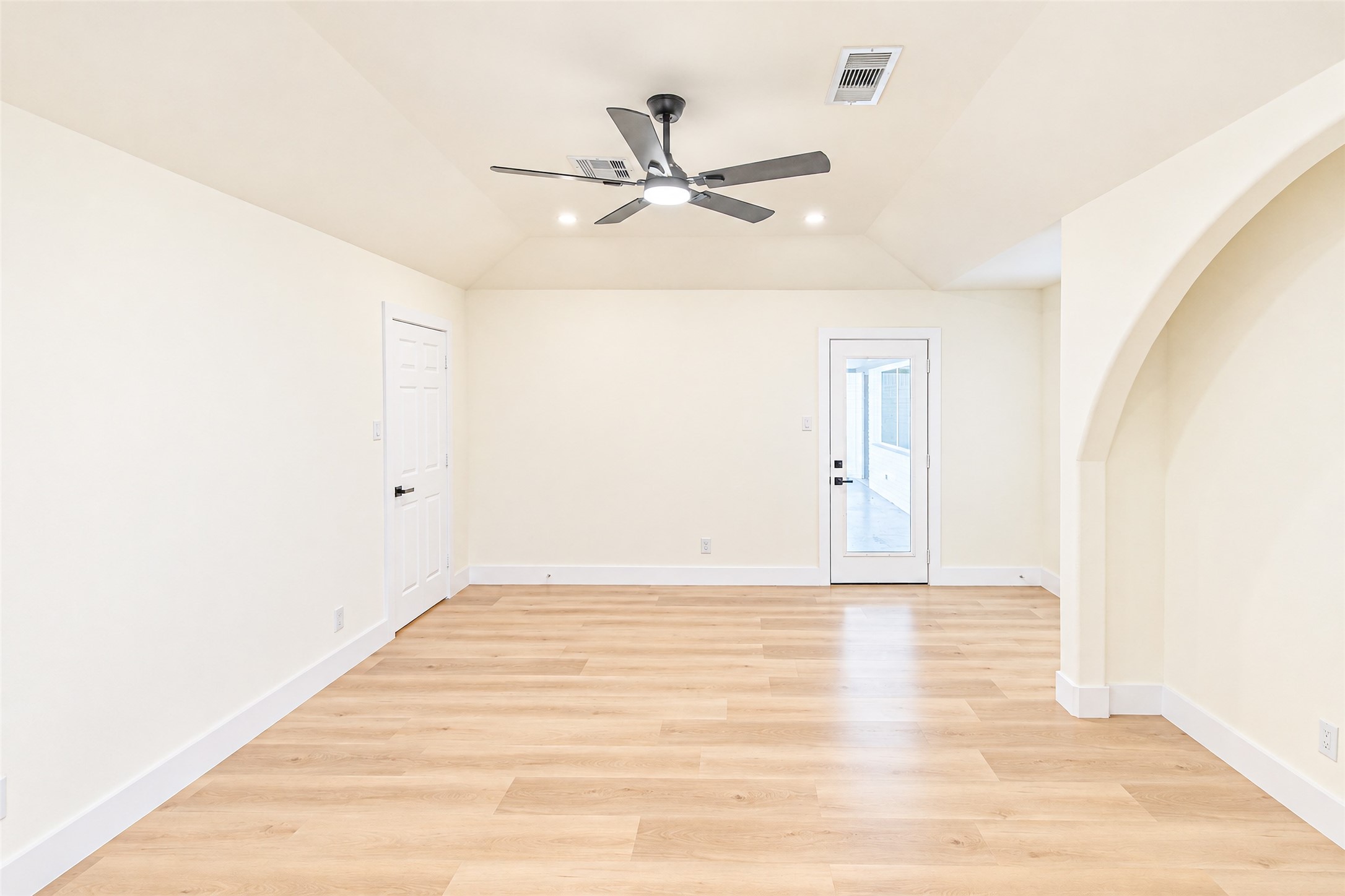 Experience the elegance of this spacious primary bedroom, featuring sleek wood flooring, a modern ceiling fan, and abundant natural light through a stylish glass door.