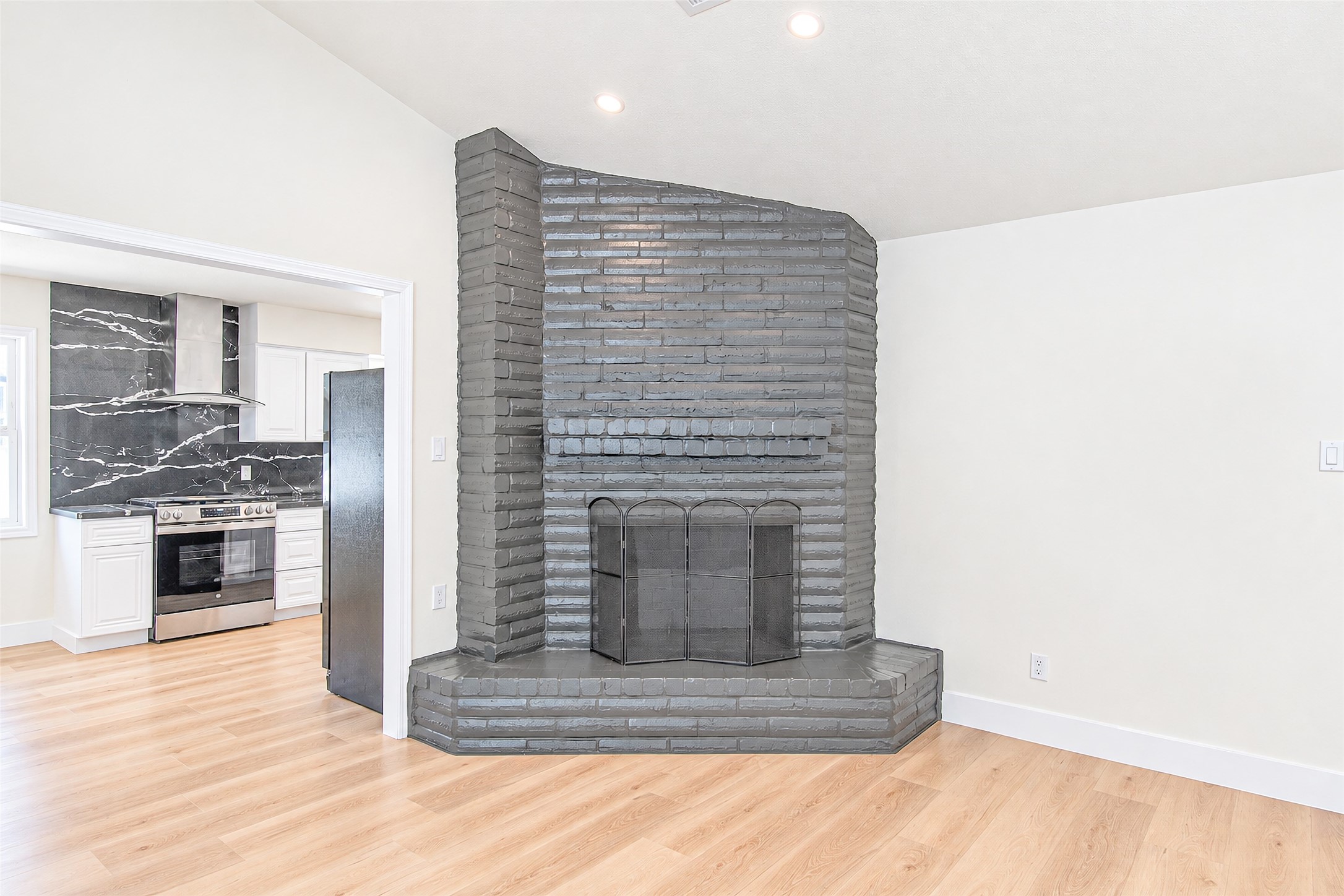 Charming living area with a striking gray brick fireplace, seamlessly flowing into a modern kitchen featuring sleek marble accents and stainless steel appliances.