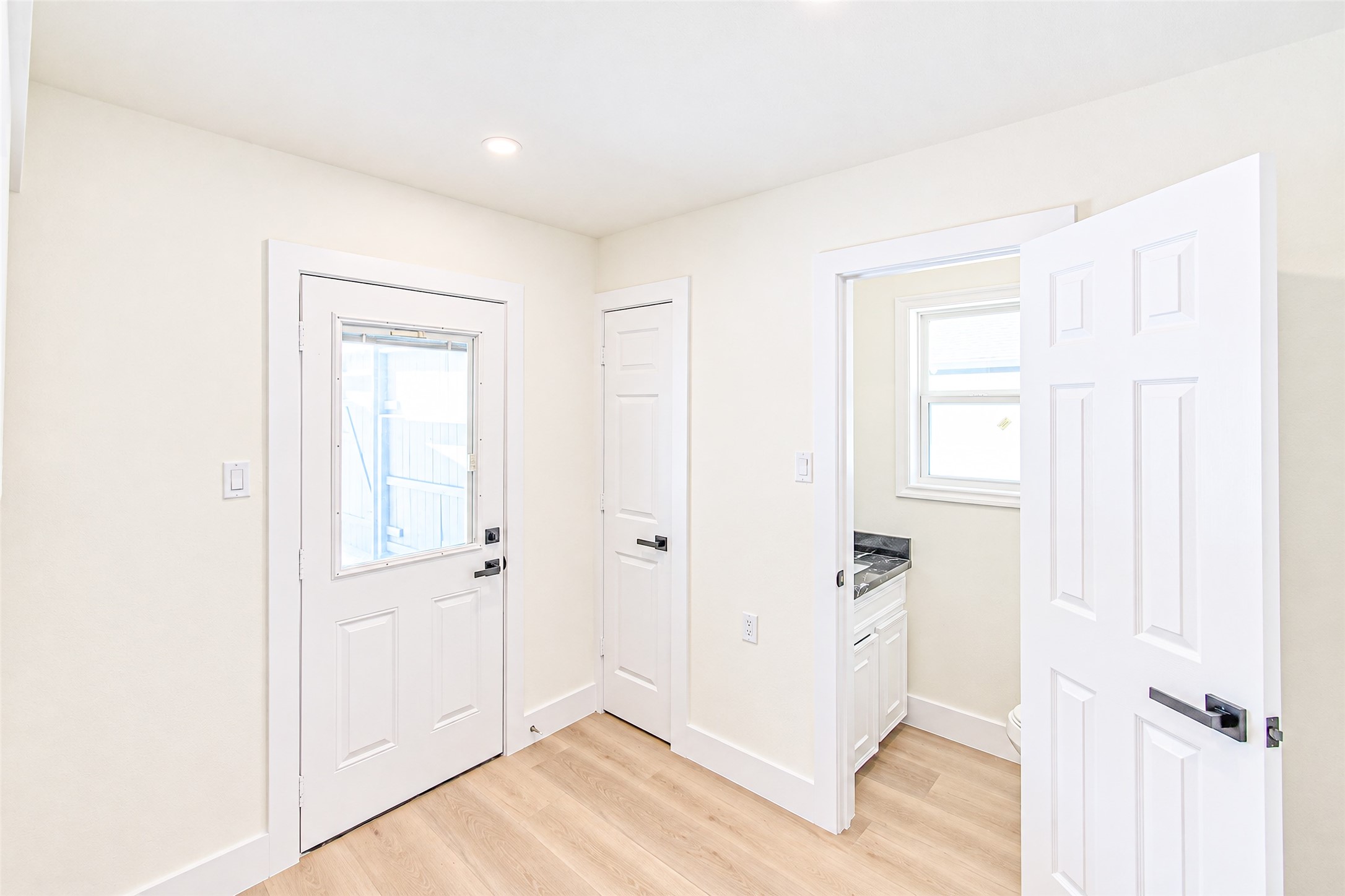 Bright and inviting space with light wood flooring, featuring a convenient side entry and a compact utility area illuminated by a small window.