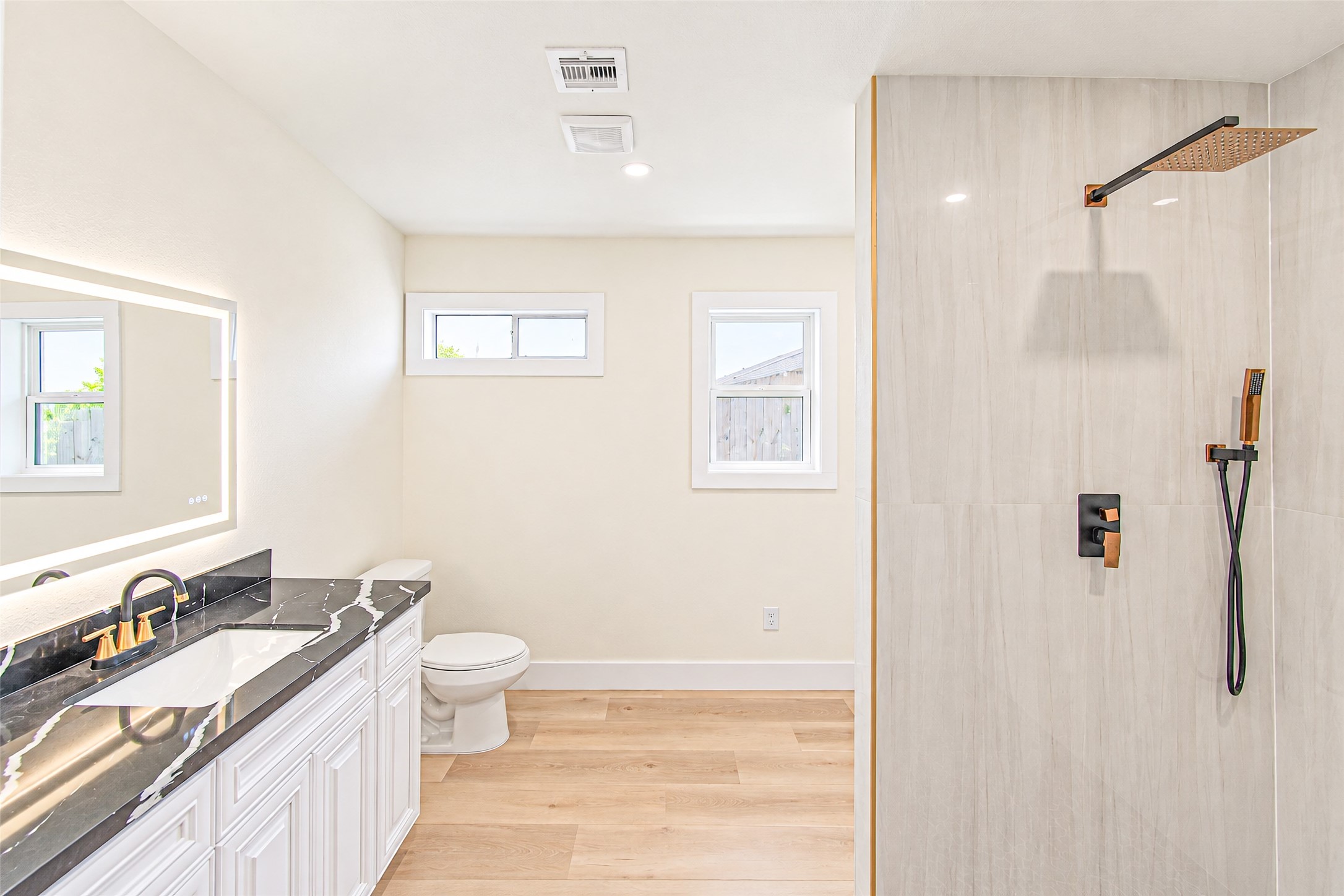 Experience luxury in the primary bath featuring a sleek, modern design with a spacious walk-in shower, elegant black marble countertops, and warm wood flooring.