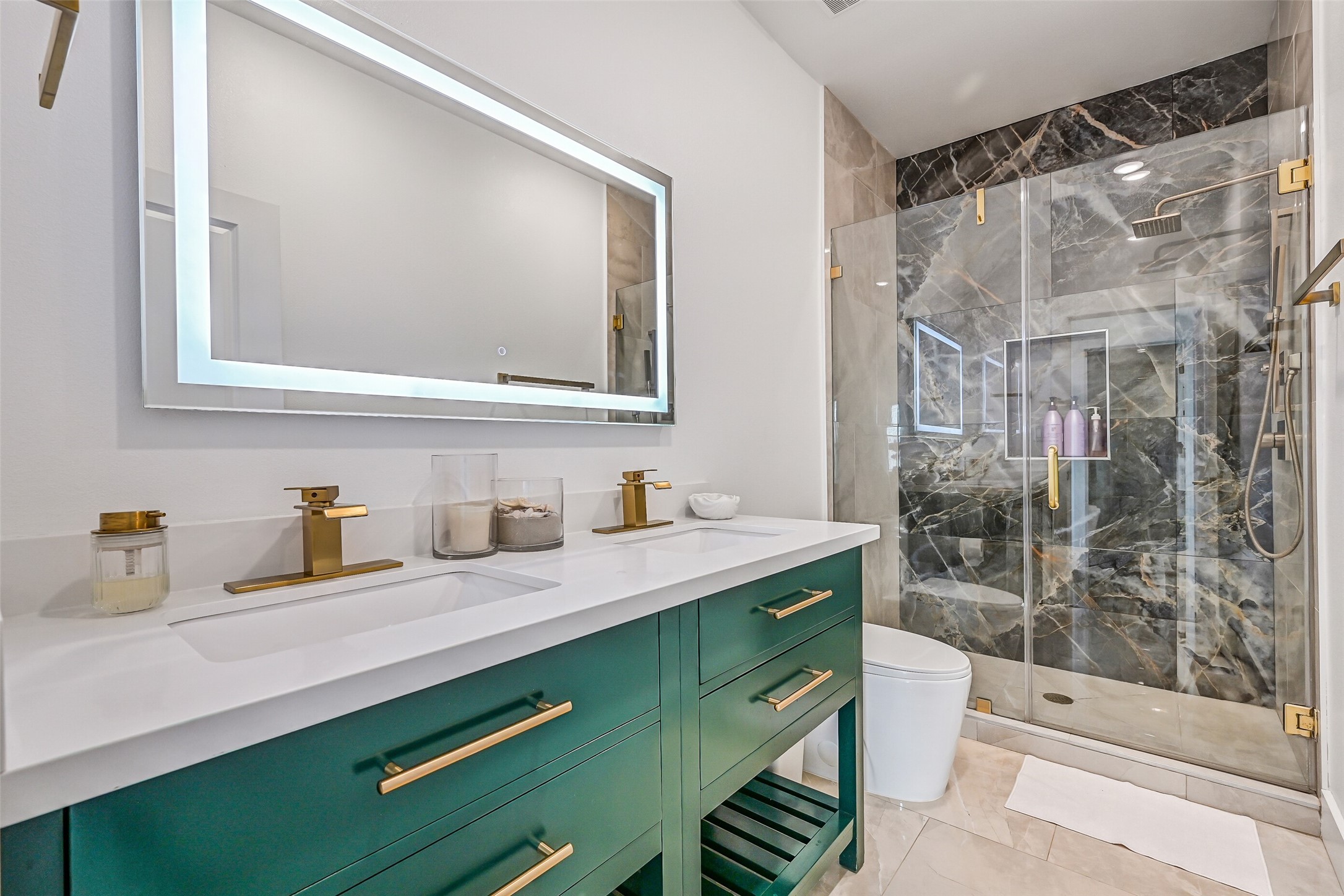 Just across the hall, youll find a similarly designed bathroom featuring elegant gold fixtures, double vanities, and a walk-in shower with stunning dark tile and a waterfall showerhead.