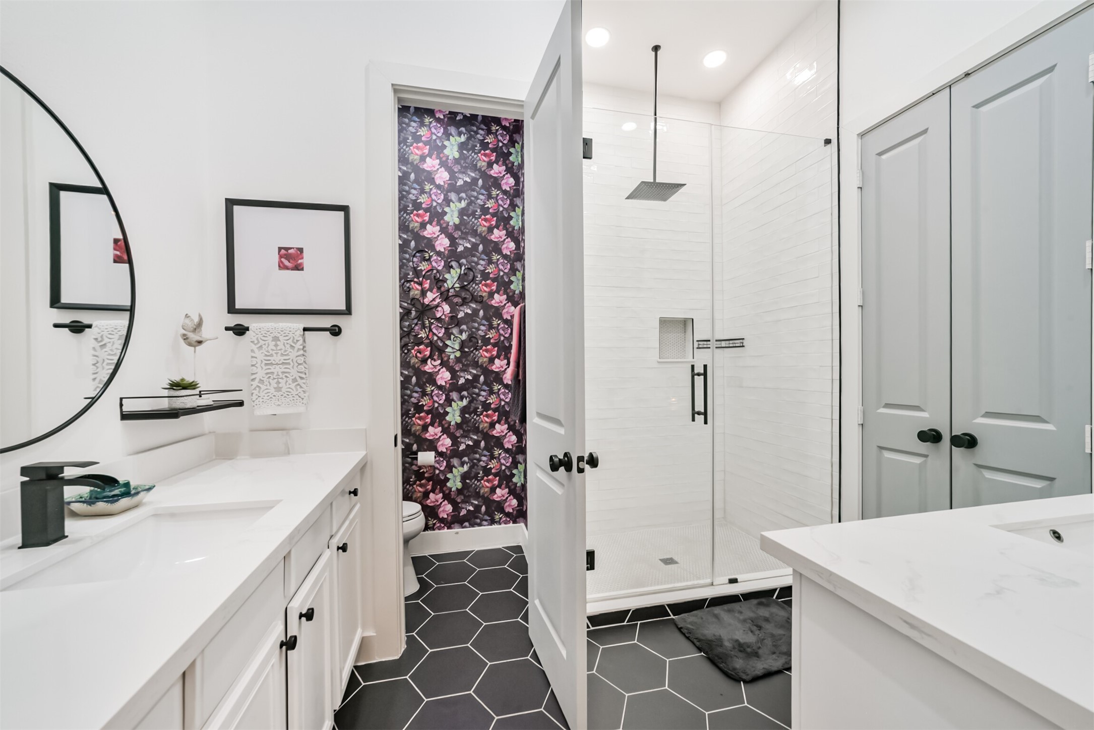 Spa-like primary bath with double sinks, quartzite counters, artisan tile surround, a rain shower and a showstopping floral wallpaper accent in water closet!
