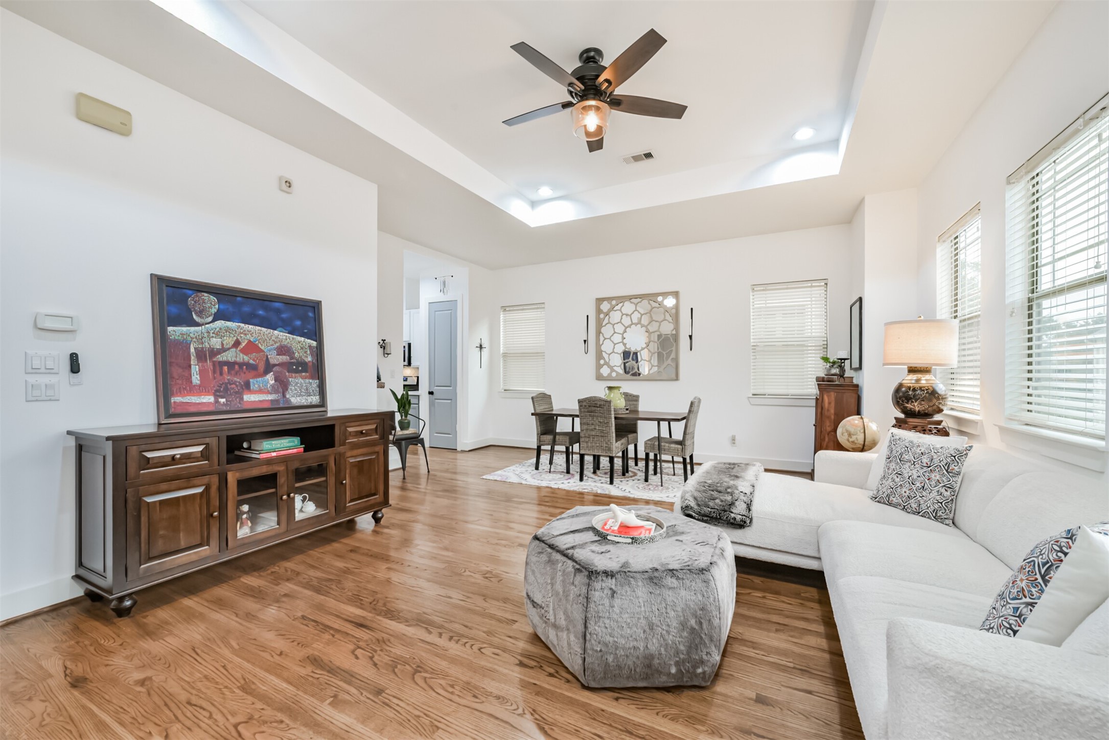 Airy, light-filled open living area with soaring tray ceiling and gleaming hardwoods