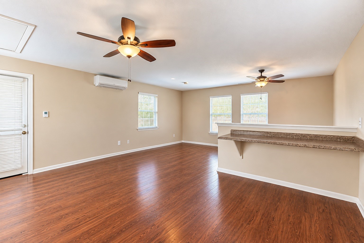 Spacious detached living area with warm wood-look flooring, ceiling fans, and ample natural light from multiple windows, offering a comfortable and inviting atmosphere.