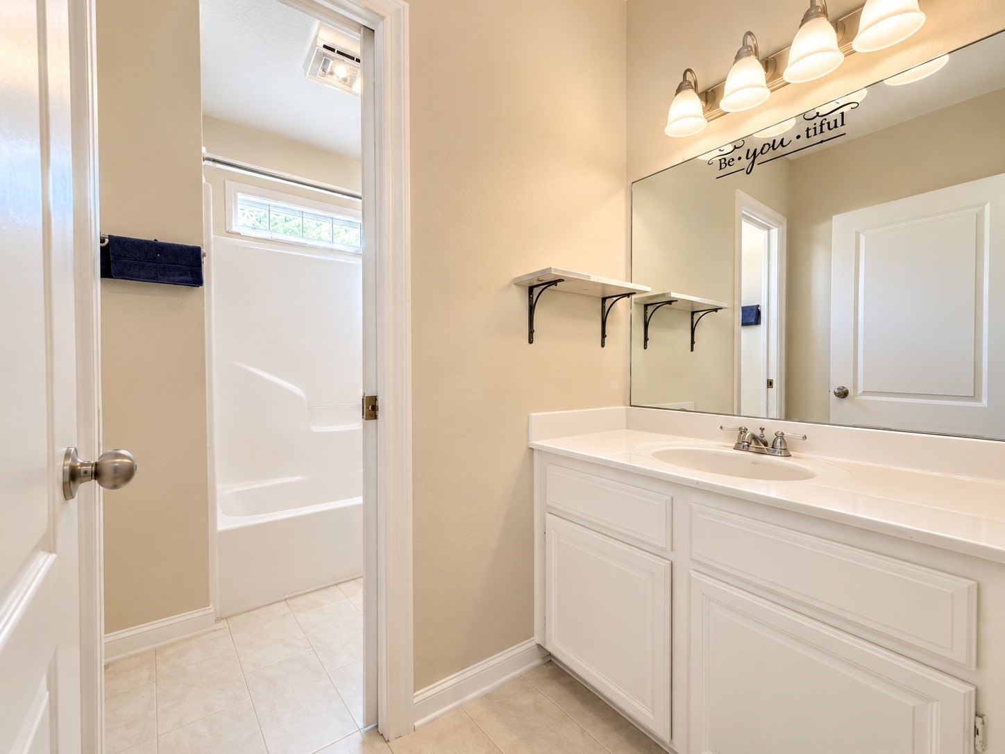 Bright and inviting secondary bathroom featuring a spacious vanity with ample storage, elegant lighting, and a convenient shower-tub combination with neutral tones.