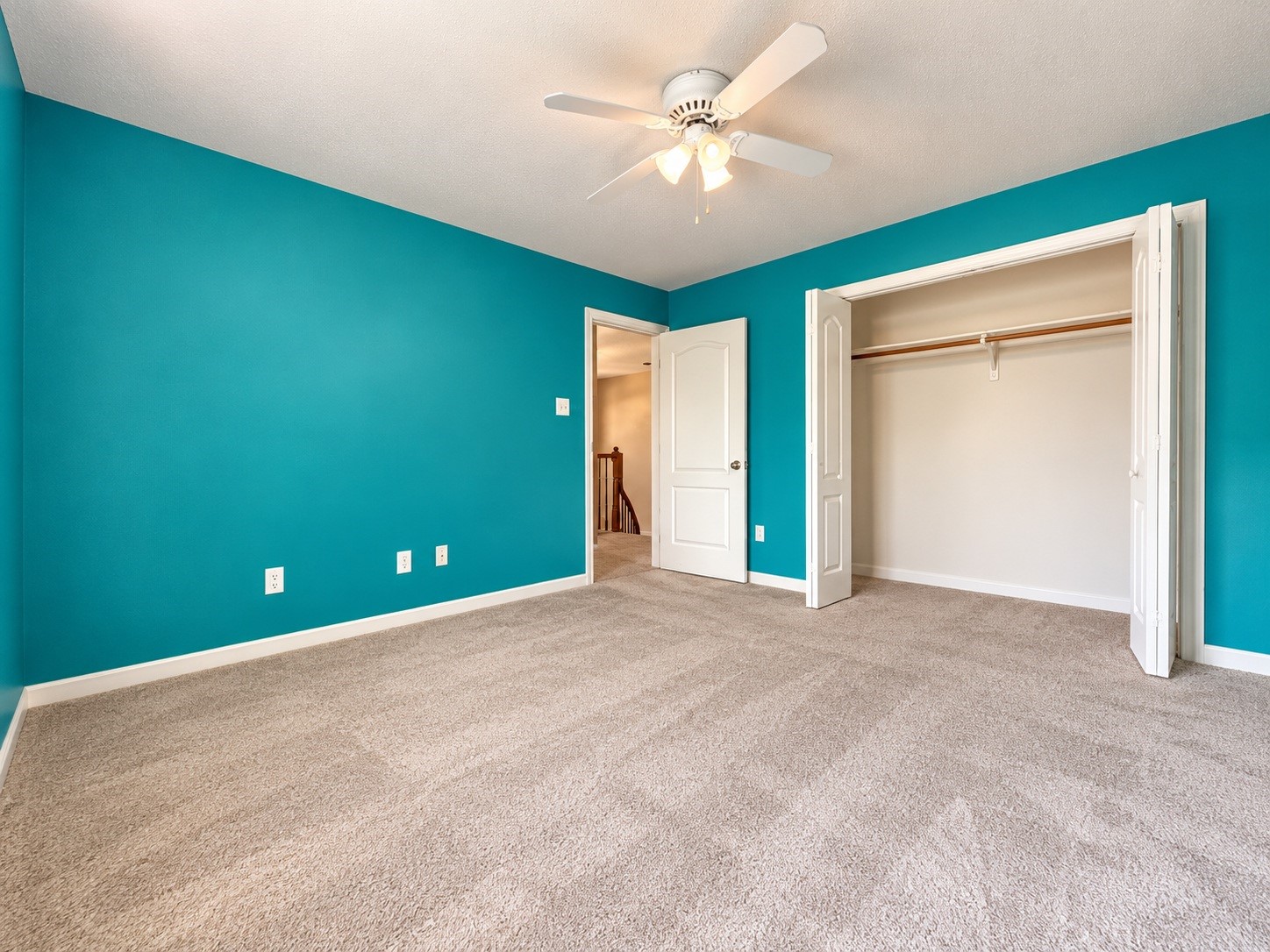 Spacious bedroom featuring vibrant teal walls, plush carpeting, a ceiling fan, and a convenient, large closet with double doors.