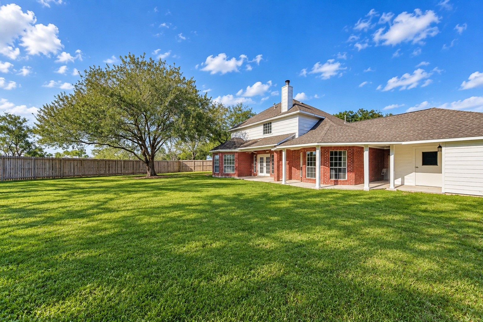 Expansive backyard with lush green lawn, mature tree, and charming red brick home featuring a spacious covered patio perfect for outdoor gatherings.
