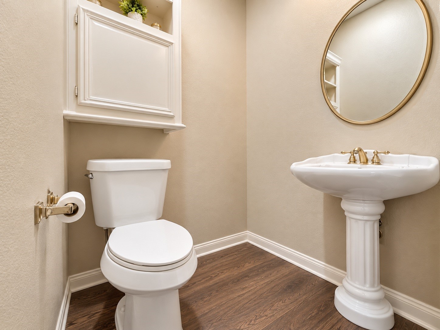 Charming powder room with elegant pedestal sink, sleek wood-look flooring, and a classic round mirror, complemented by a convenient storage cabinet.