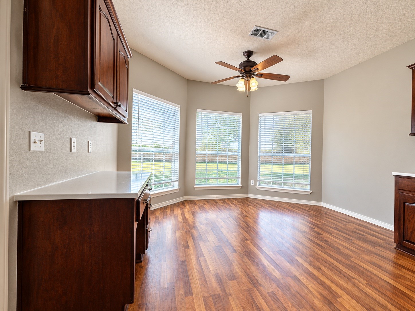 Bright breakfast area with large windows, wood-look floors, and a ceiling fan, offering an inviting space for meals and gatherings.