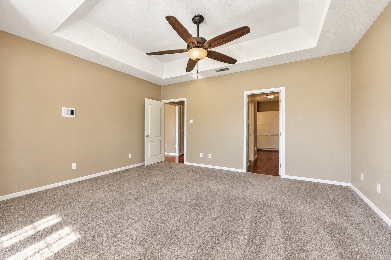 Spacious master bedroom featuring a tray ceiling, ceiling fan, and plush carpet, with convenient access to the en-suite master bathroom.