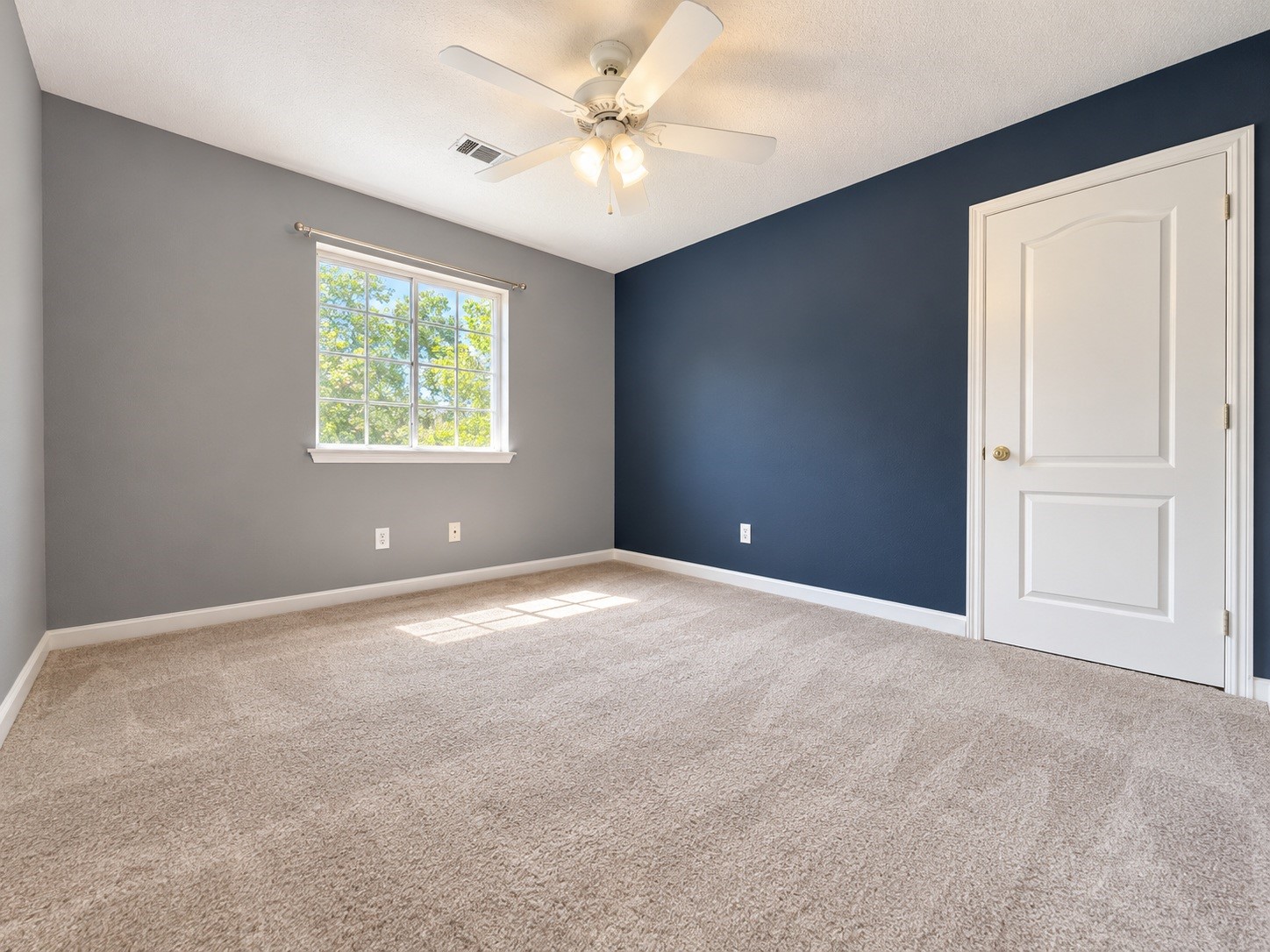 Spacious bedroom featuring plush carpeting, a modern ceiling fan, and abundant natural light through a large window.