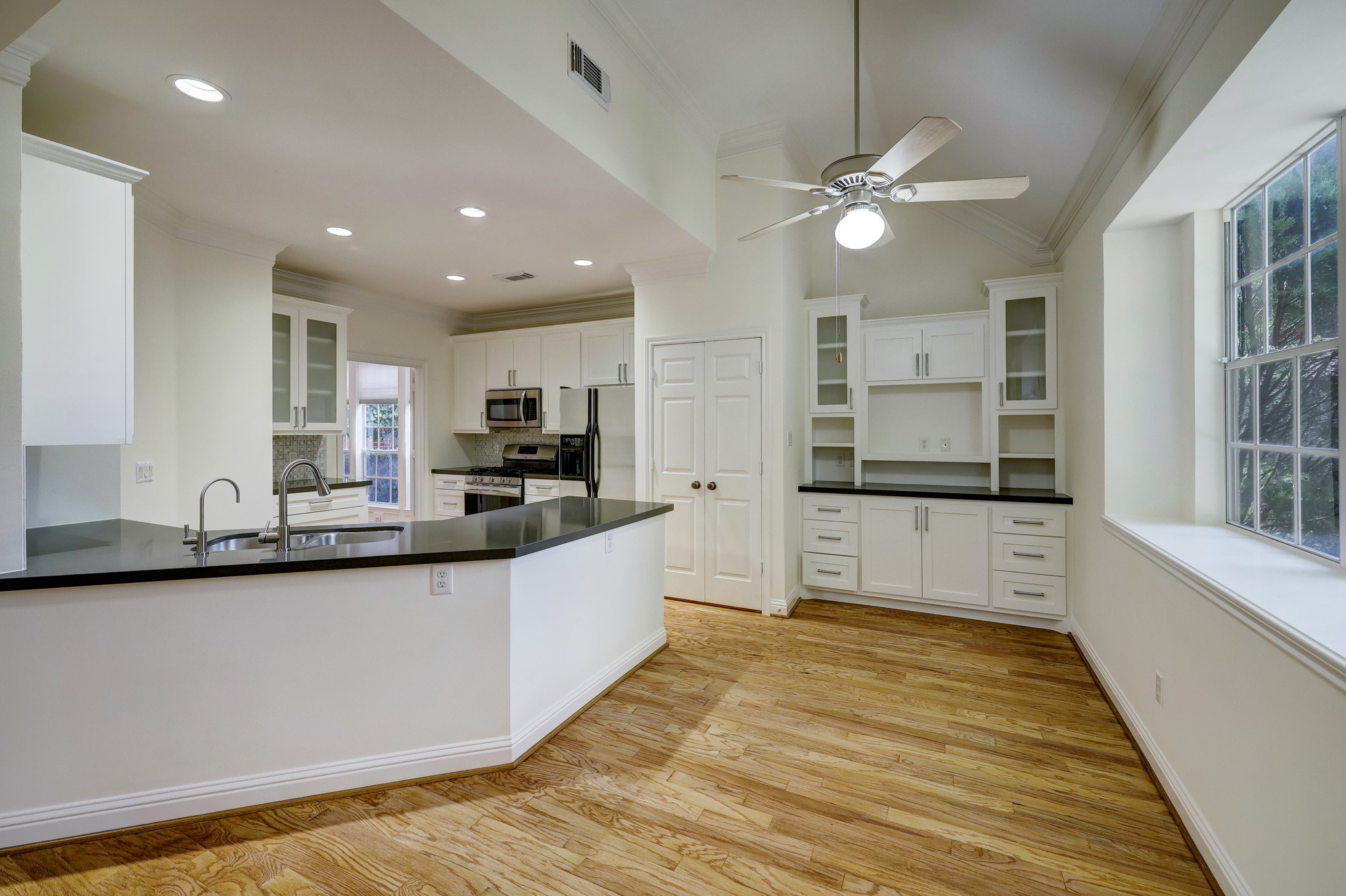 KITCHEN & BREAKFAST ROOM: Bright and functional space featuring new stainless steel dishwasher and refrigerator, white cabinetry with glass-front uppers, sleek black countertops, and a central island with double sink. The breakfast area offers built-in storage and large windows for abundant natural light.