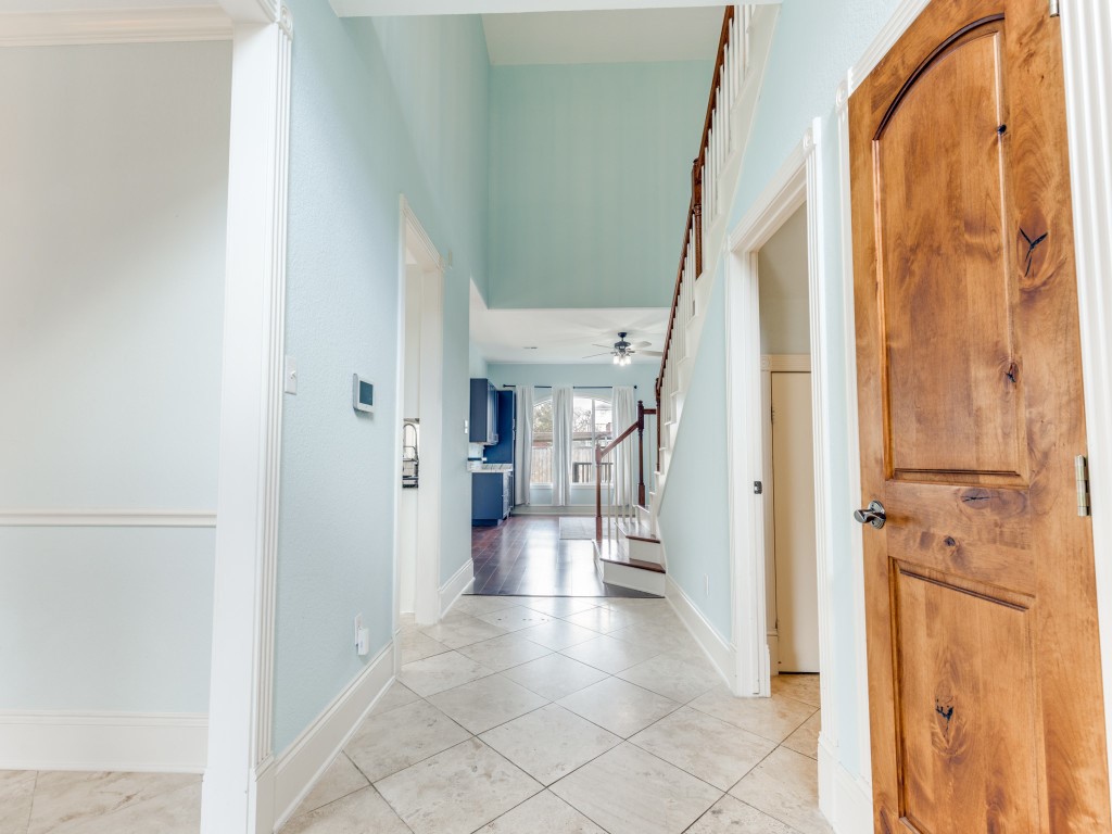 This inviting entryway features light blue walls, tiled flooring, and a wooden staircase leading to the second floor. The space opens up to a bright area with large windows and access to the kitchen, showcasing a blend of tile and wooden elements for a warm, welcoming feel. This inviting entryway features light blue walls, tiled flooring, and a wooden staircase leading to the second floor. The space opens up to a bright area with large windows and access to the kitchen, showcasing a blend of tile and wooden elements for a warm, welcoming feel.