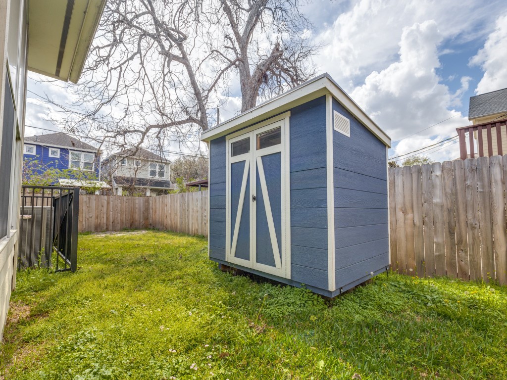 This backyard features a small blue storage shed with white trim, set on a grassy area enclosed by a wooden fence, providing a private and functional storage space.