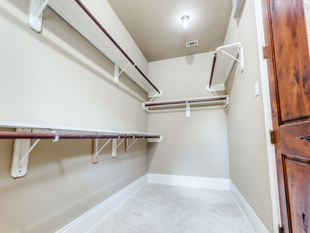 Primary walk-in closet is spacious with ample shelving and hanging space, featuring neutral walls, a light fixture, and a hard wood door.