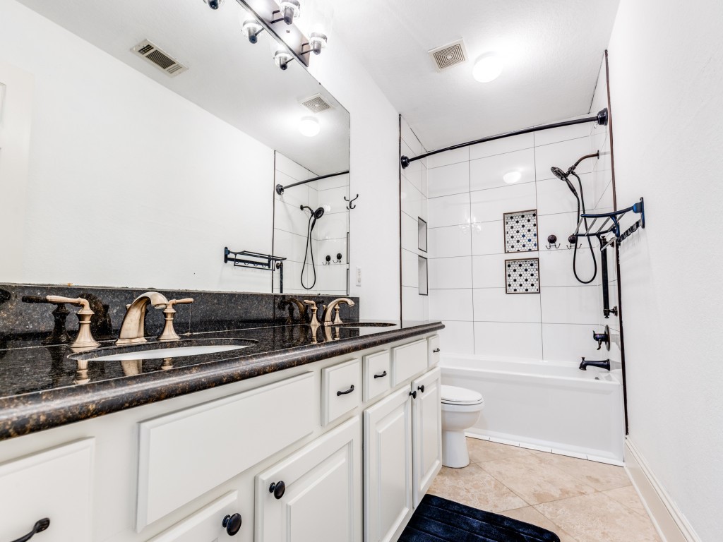 This bathroom features a modern design with a spacious double vanity, sleek granite countertops, and elegant fixtures. The shower-tub combination is accented with stylish tile work, and the room is well-lit with contemporary lighting.