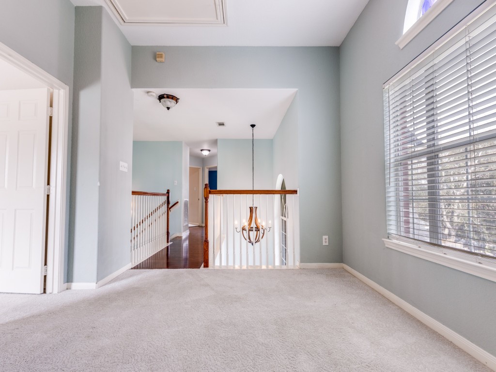 Bright and airy upper hallway with carpet flooring, large window with blinds, and a view of the staircase. Features a hanging light fixture and light-colored walls, creating an inviting and open feel.