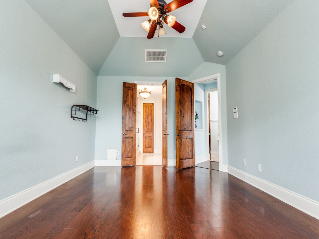 Another view of the Primary bedroom which features a vaulted ceiling, rich hardwood floors, and soft blue walls. It has elegant wooden double doors leading to the primary bathroom area.