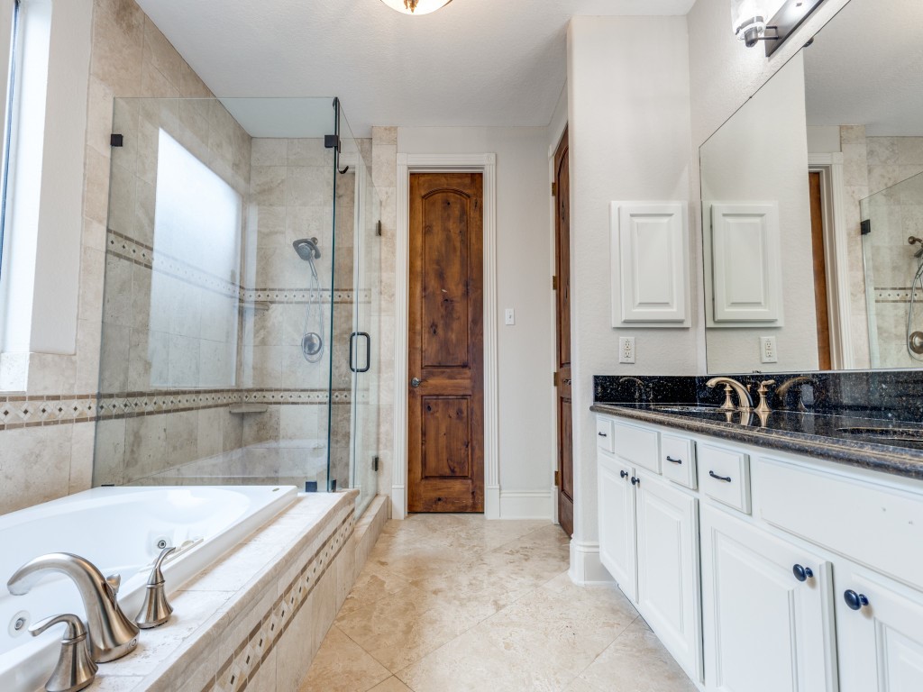 The primary bathroom features a luxurious design with a large glass-enclosed shower, a soaking tub, and elegant fixtures. The double vanity has a sleek black countertop, and the room is finished with neutral-toned tiles and a wooden door, creating a sophisticated and inviting space.