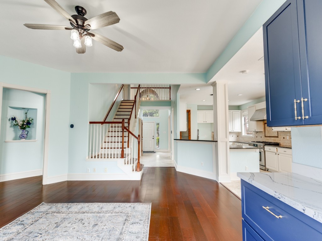 This photo showcases a bright, open living area with hardwood floors. The space includes a modern bar with built in wine fridge, blue cabinets and a marble countertop, adjacent to a staircase leading to the upper level, providing a spacious and inviting atmosphere. This photo showcases a bright, open living area with hardwood floors. The space includes a modern bar with built in wine fridge, blue cabinets and a marble countertop, adjacent to a staircase leading to the upper level, providing a spacious and inviting atmosphere.