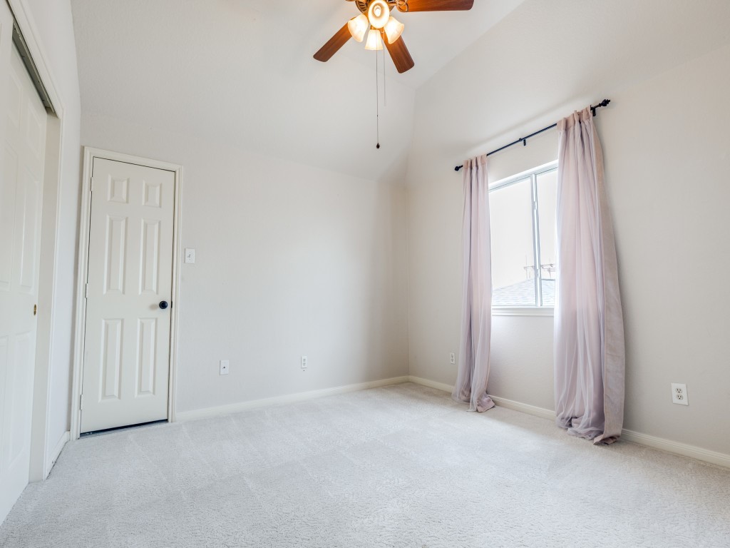 3rd bedroom on 2nd floor features a neutral color palette with plush carpeting, a ceiling fan, and ample natural light from the window with sheer curtains. A door leads to additional space or storage.