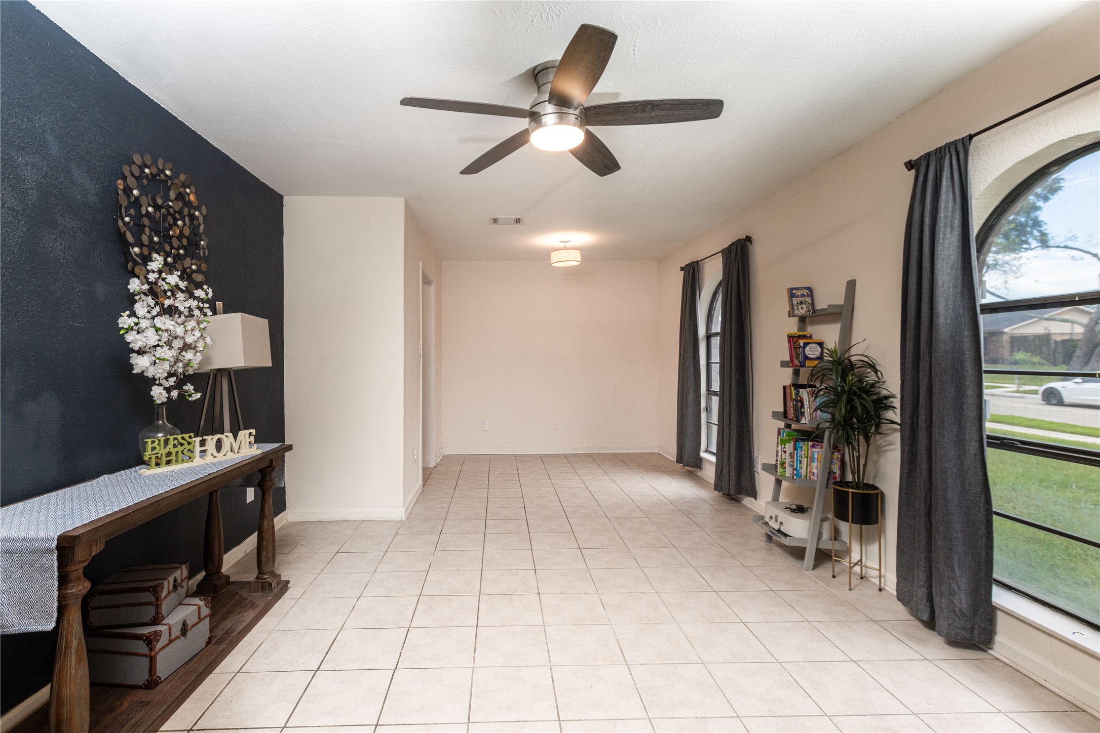Bright and airy room with large arched windows, stylish tile flooring, and a modern ceiling fan.