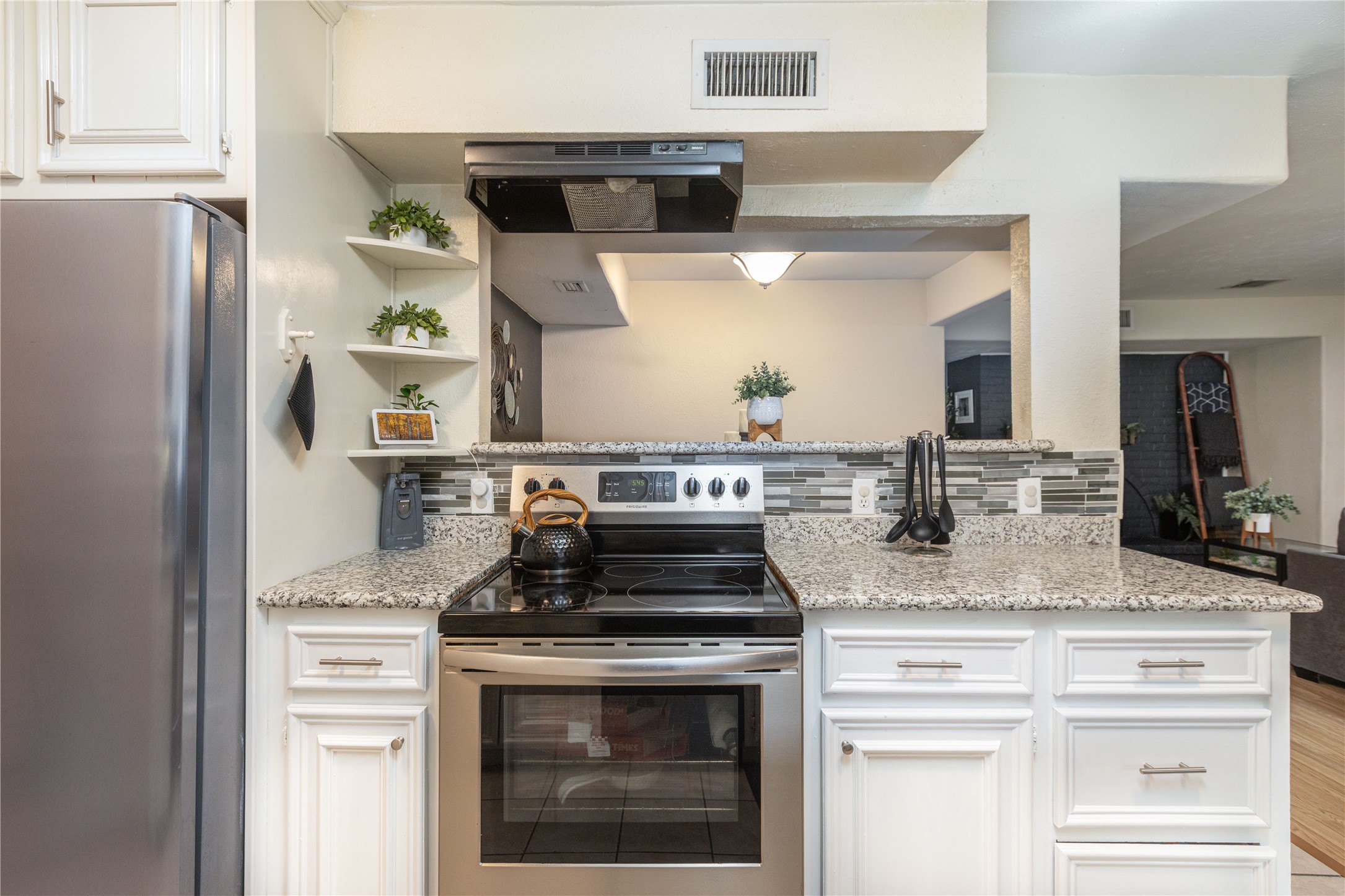 Modern kitchen with sleek stainless steel appliances, granite countertops, and stylish open shelving for a functional and elegant cooking space.