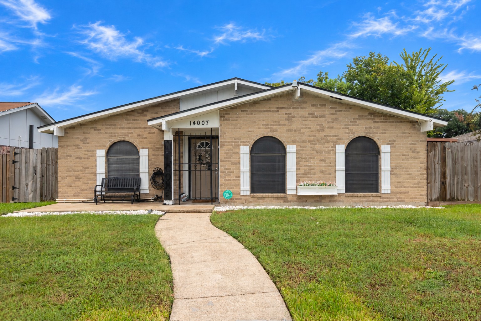 Charming single-story home with a welcoming curved walkway, featuring a cozy front porch and beautiful arched windows, all surrounded by a well-maintained lawn.