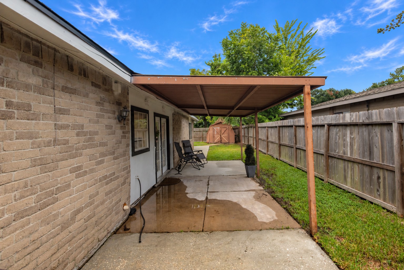 Charming covered patio area with cozy seating, perfect for relaxing, leads to a private fenced yard with a storage shed.
