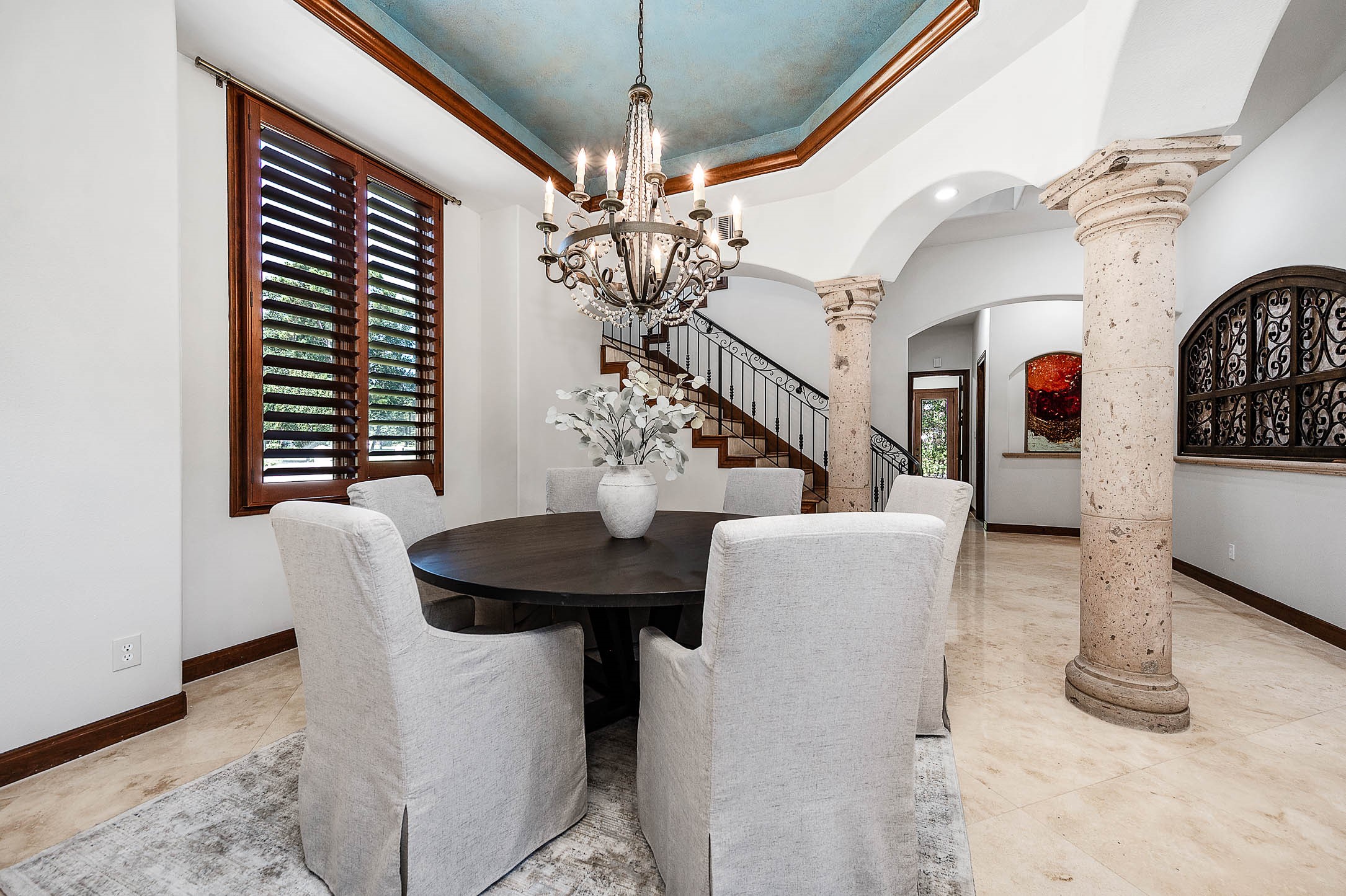 The formal dining room is defined by Cantera stone columns, a statement chandelier, and a domed tray ceiling with a decorative painted finish.
