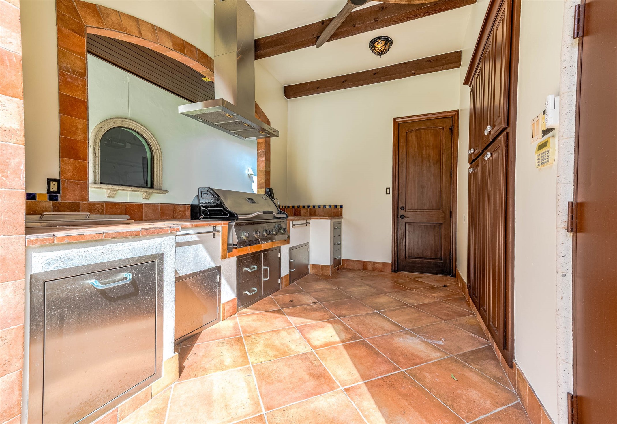 The summer kitchen features a built-in grill, a stainless steel vent hood, and exposed wood beams.