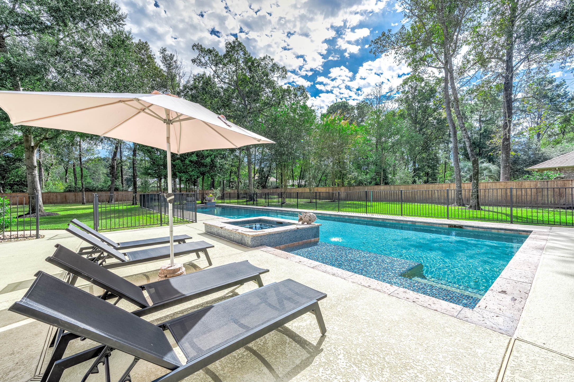 The pool deck offers ample space for lounging beneath large mature trees.