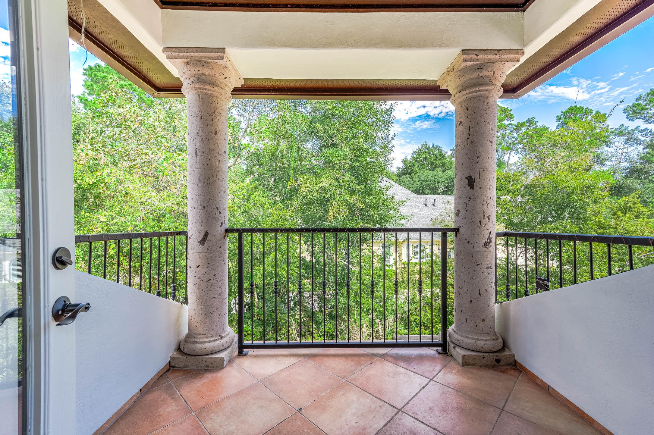 A covered balcony with Cantera stone columns overlooks the mature tree canopy.