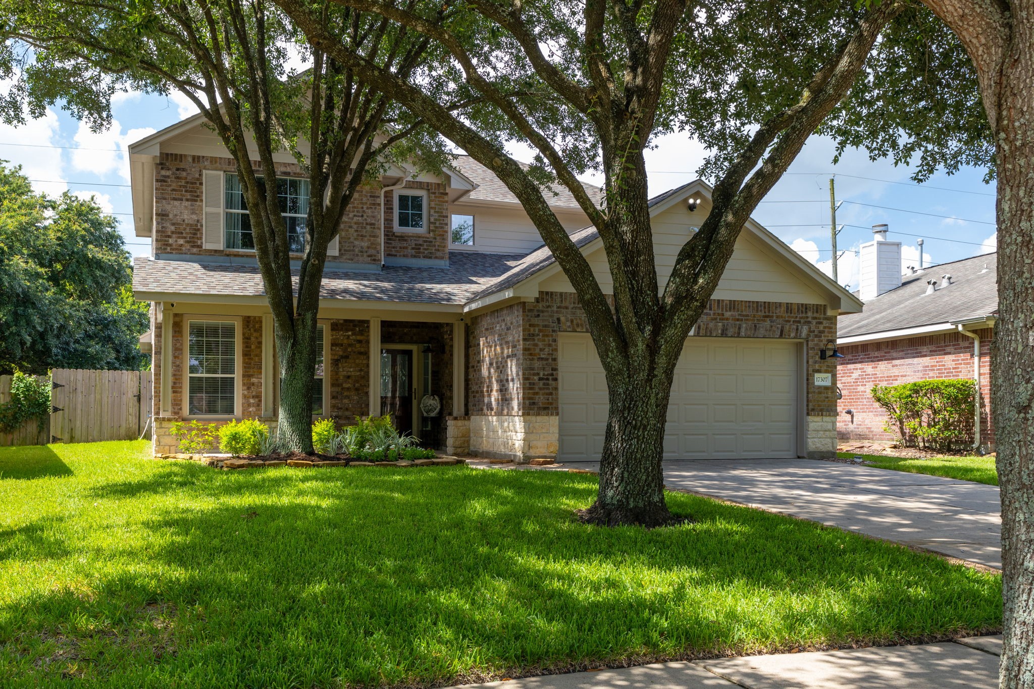 This is a charming two-story brick home with a well-maintained front yard and mature trees. It features a two-car garage and a welcoming front entrance.