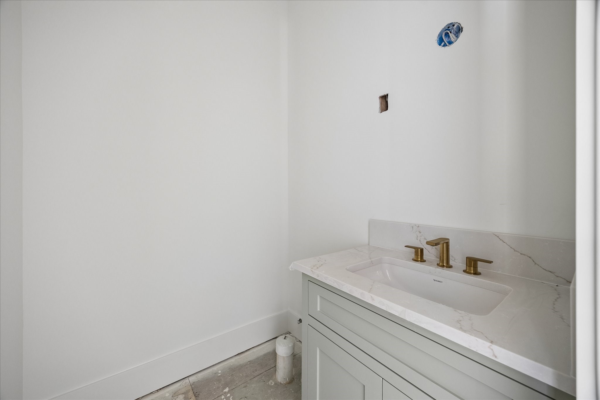 Rectangular basin, veined counter and brass tone faucet create a warm contrast against the light vanity and walls. Enclosed cabinet storage sits below the basin, keeping daily supplies close at hand. Mirror and final lighting installation remain in progress.